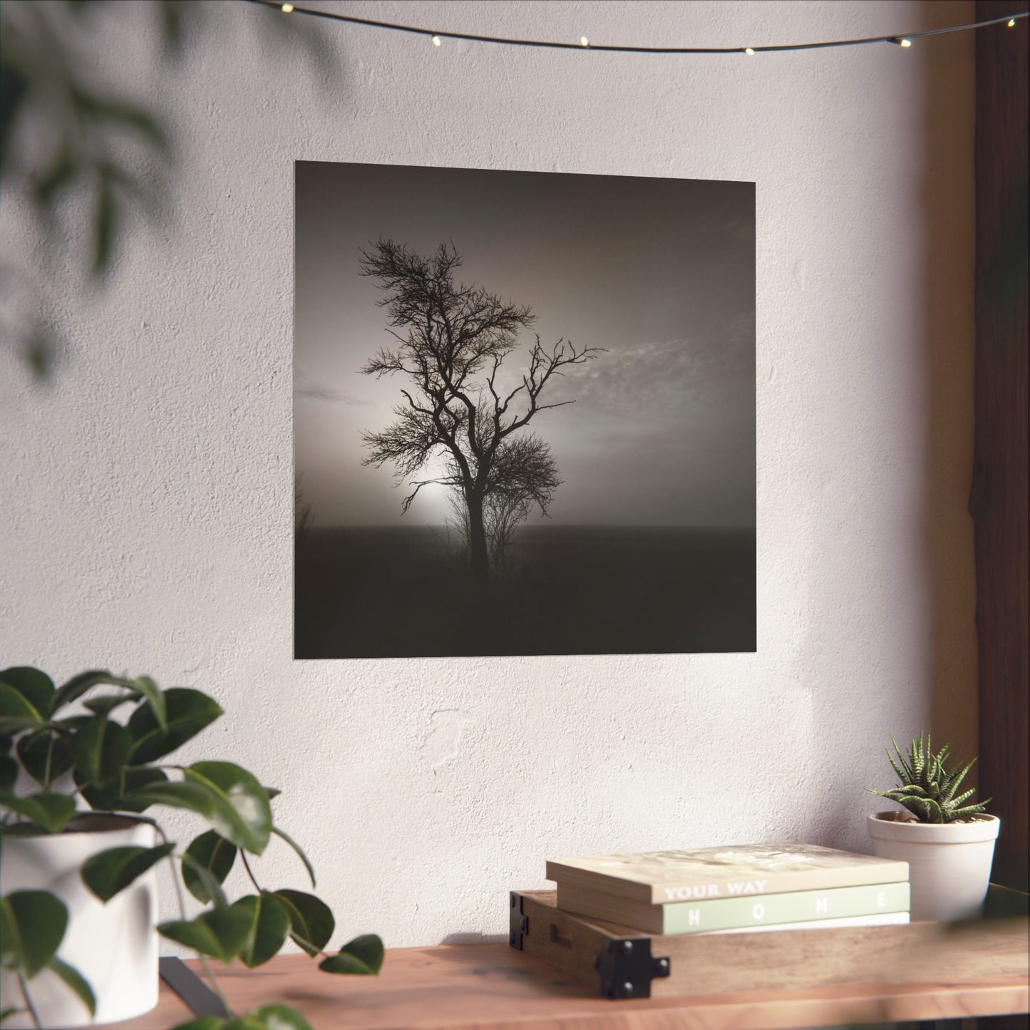 Art print of a tree on a wall above a wooden desk with plants and books.