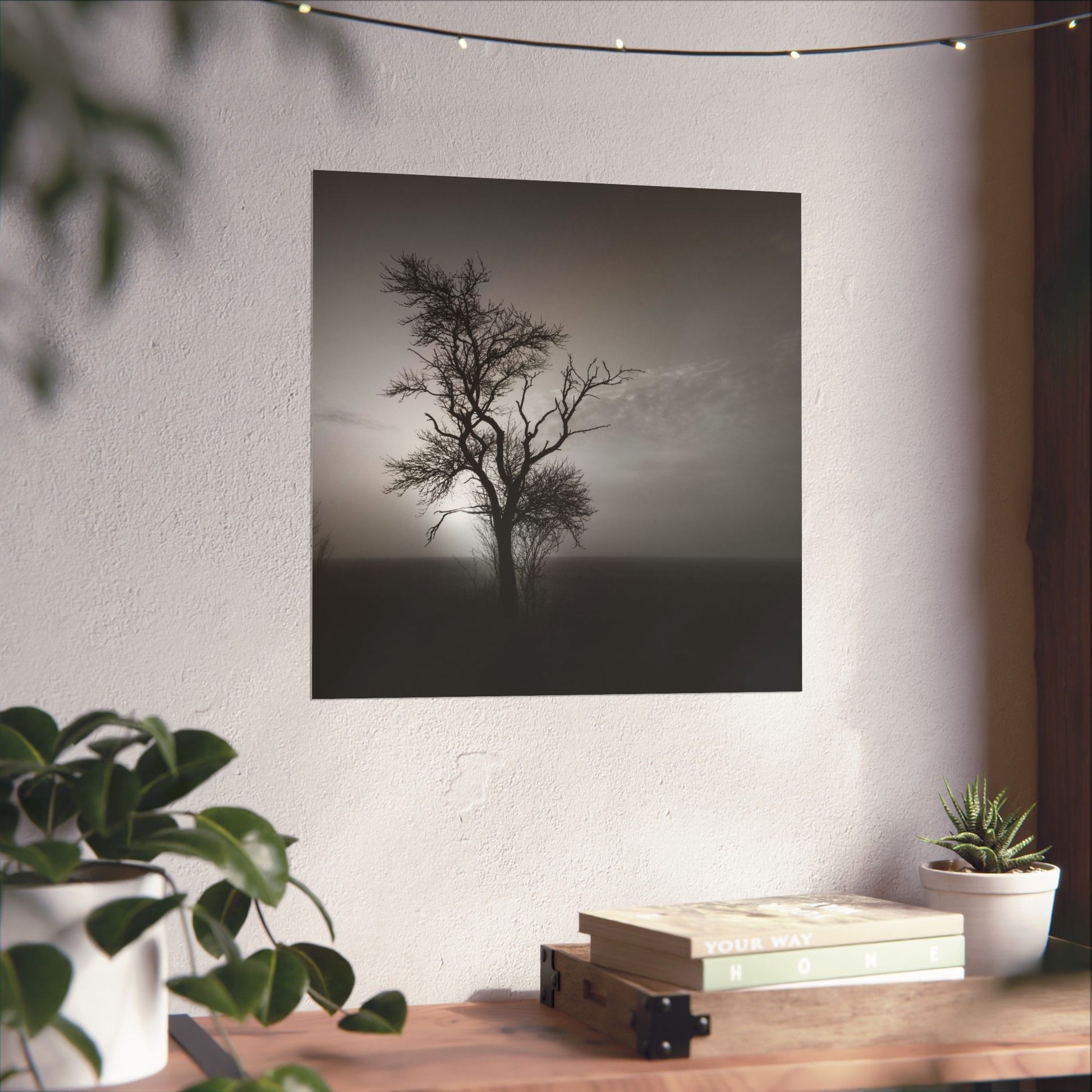 Art print of a tree on a wall above a wooden desk with plants and books.
