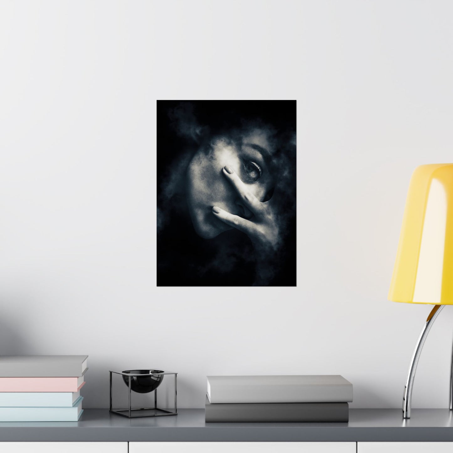 Framed artwork of a stylized face on a wall above a shelf with books and a lamp.
