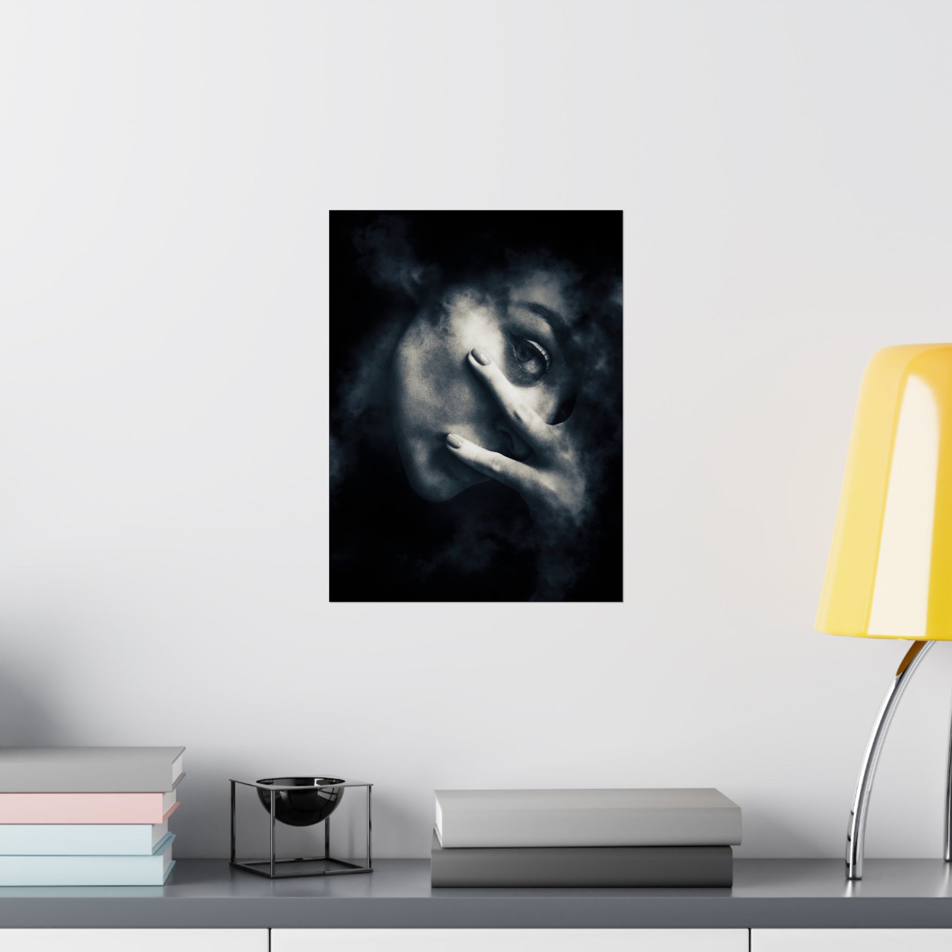 Framed artwork of a stylized face on a wall above a shelf with books and a lamp.