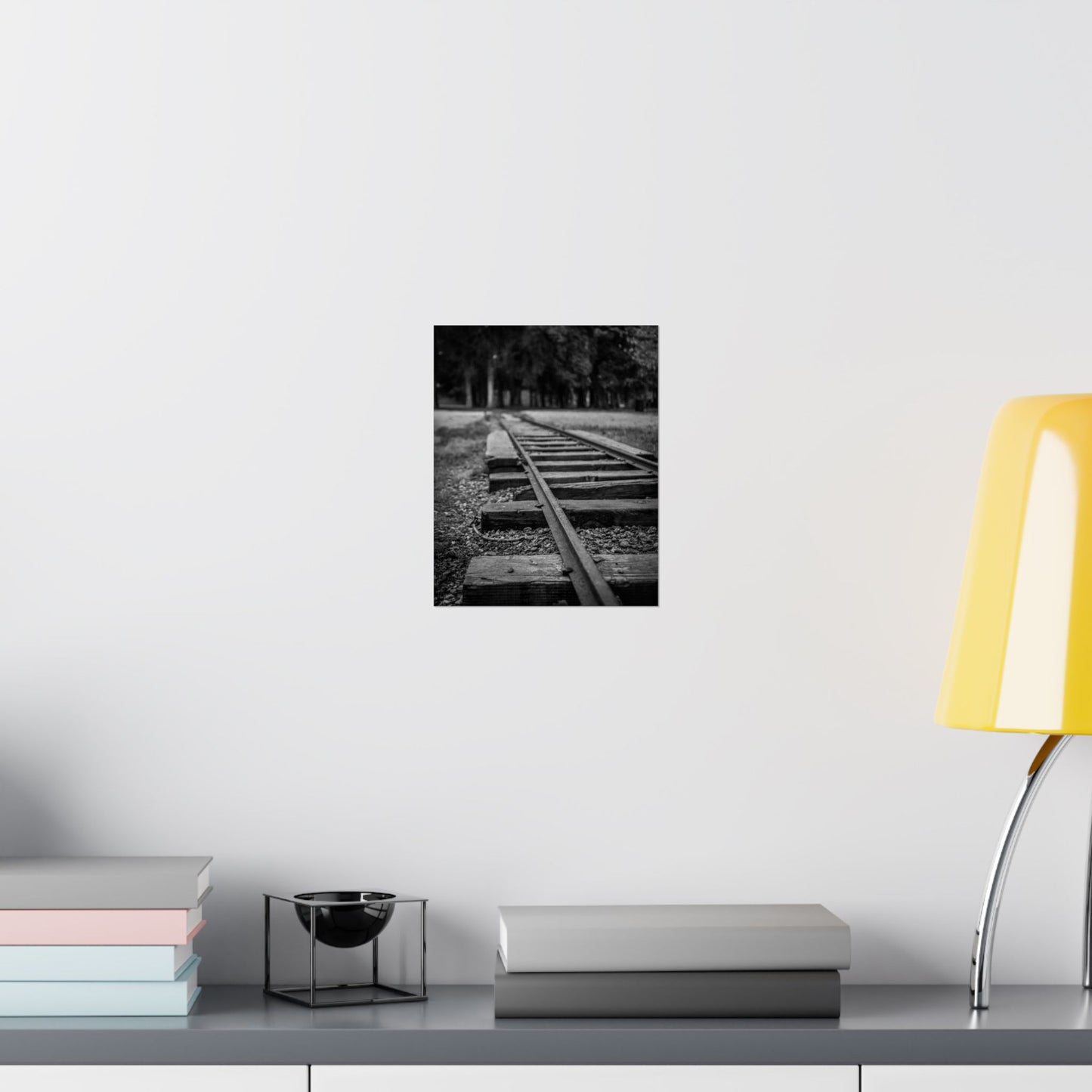 Poster of a black and white landscape with trees on a wall above a desk with books and a lamp.