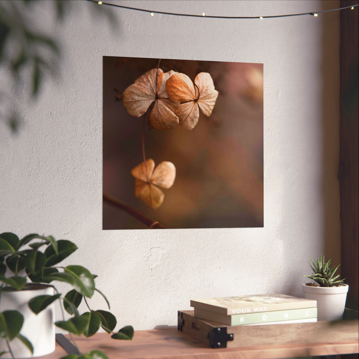 Decorative wall art of dried flowers on a white wall with a wooden table and plants below.