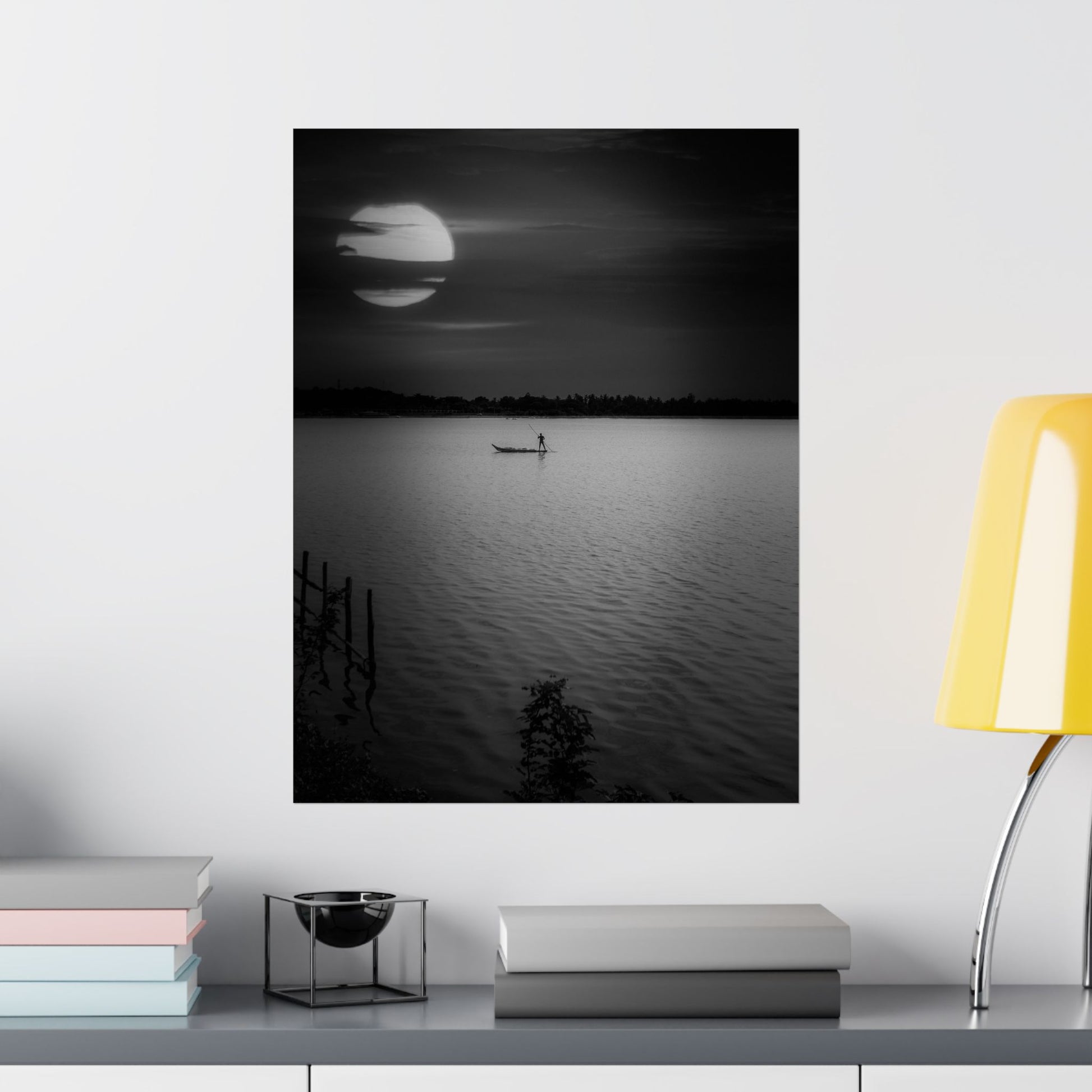 Framed black and white artwork of a moonlit lake with a canoe, displayed on a wall above a shelf.