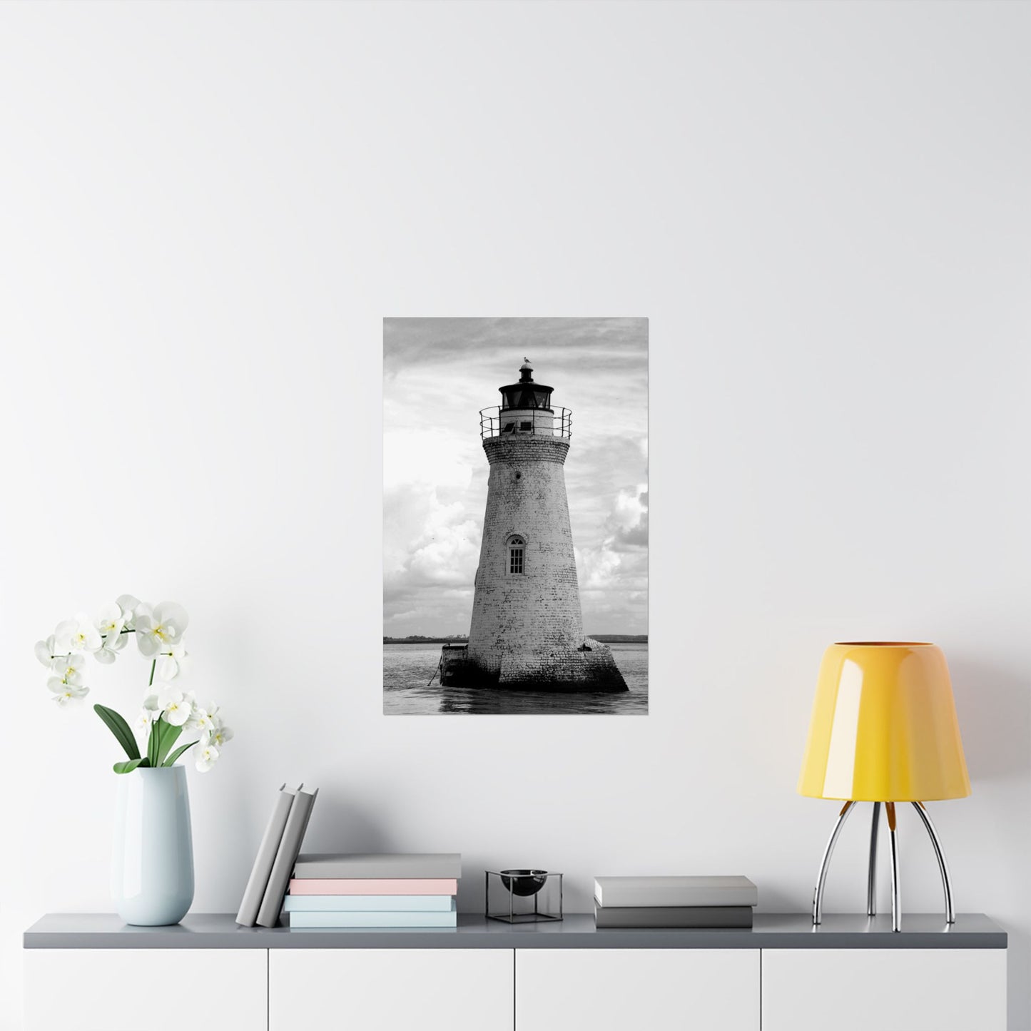 Framed black and white lighthouse print on a wall above a shelf with decor items.