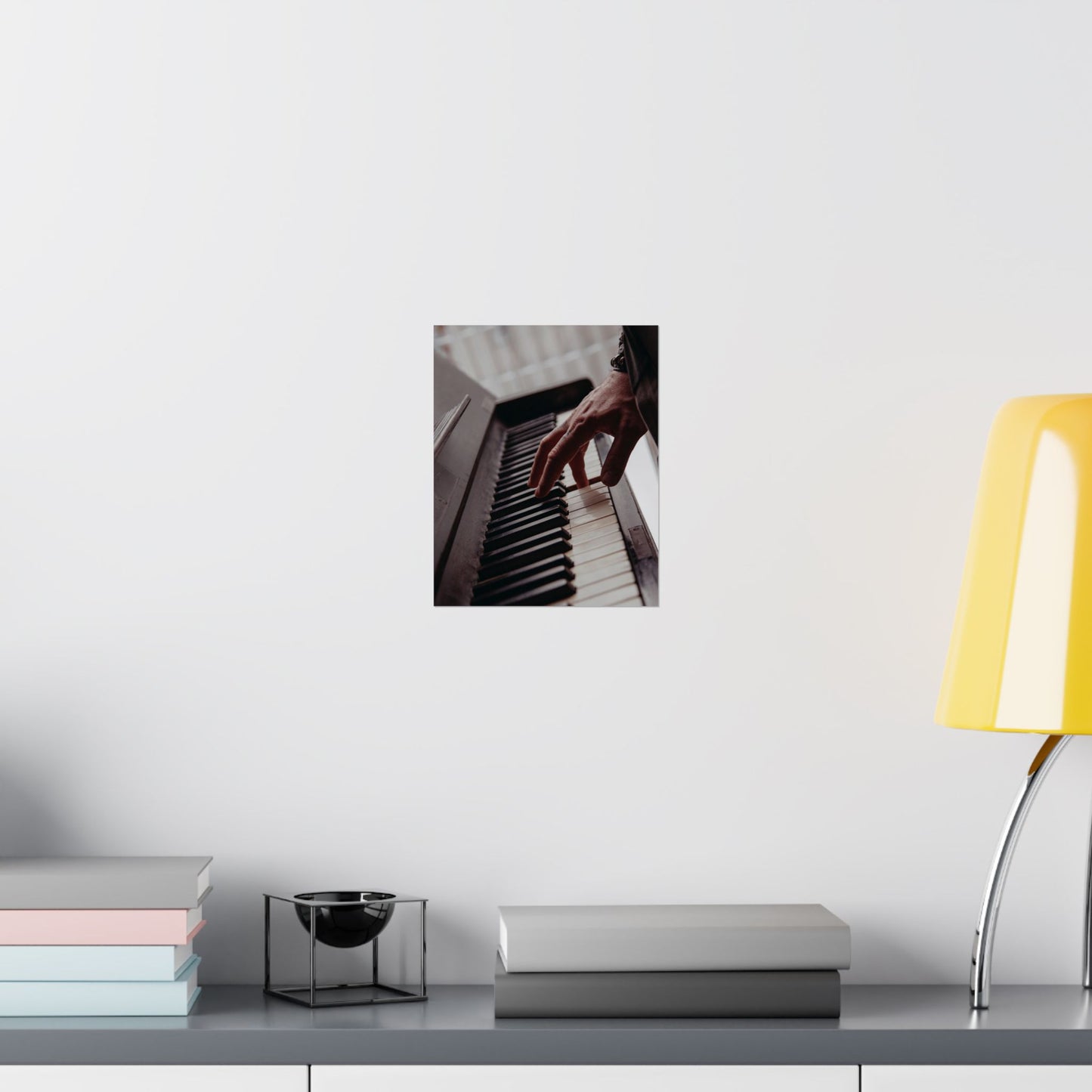 Framed photo of hands playing piano on a wall above a desk with books and a lamp.