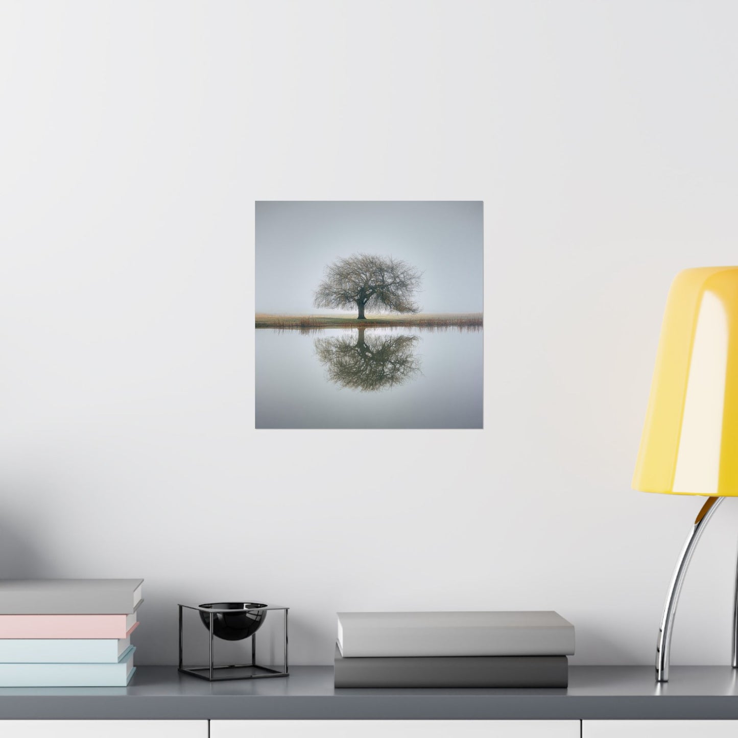 Wall art of a tree reflected in water on a white wall above a shelf with books and decor.