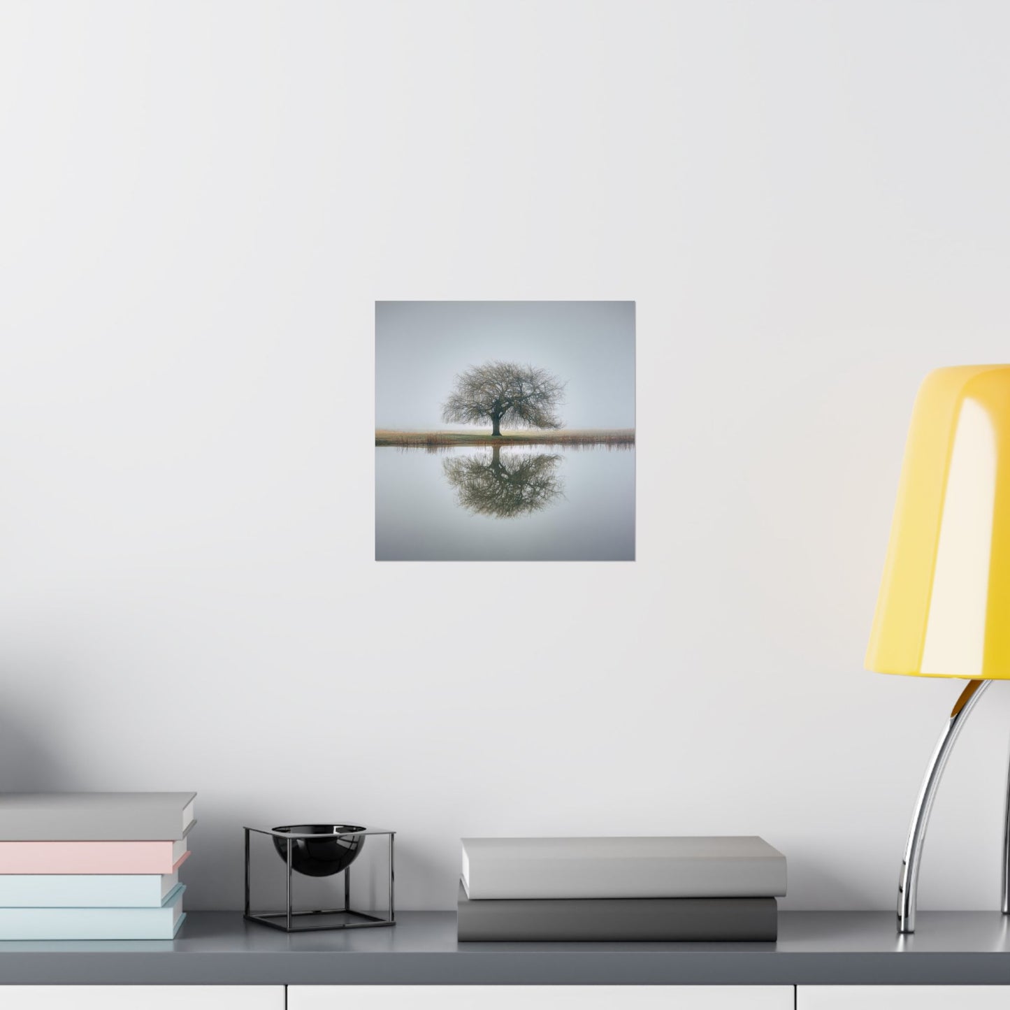 Framed artwork of a tree reflected in water on a wall above a desk with books and a lamp.
