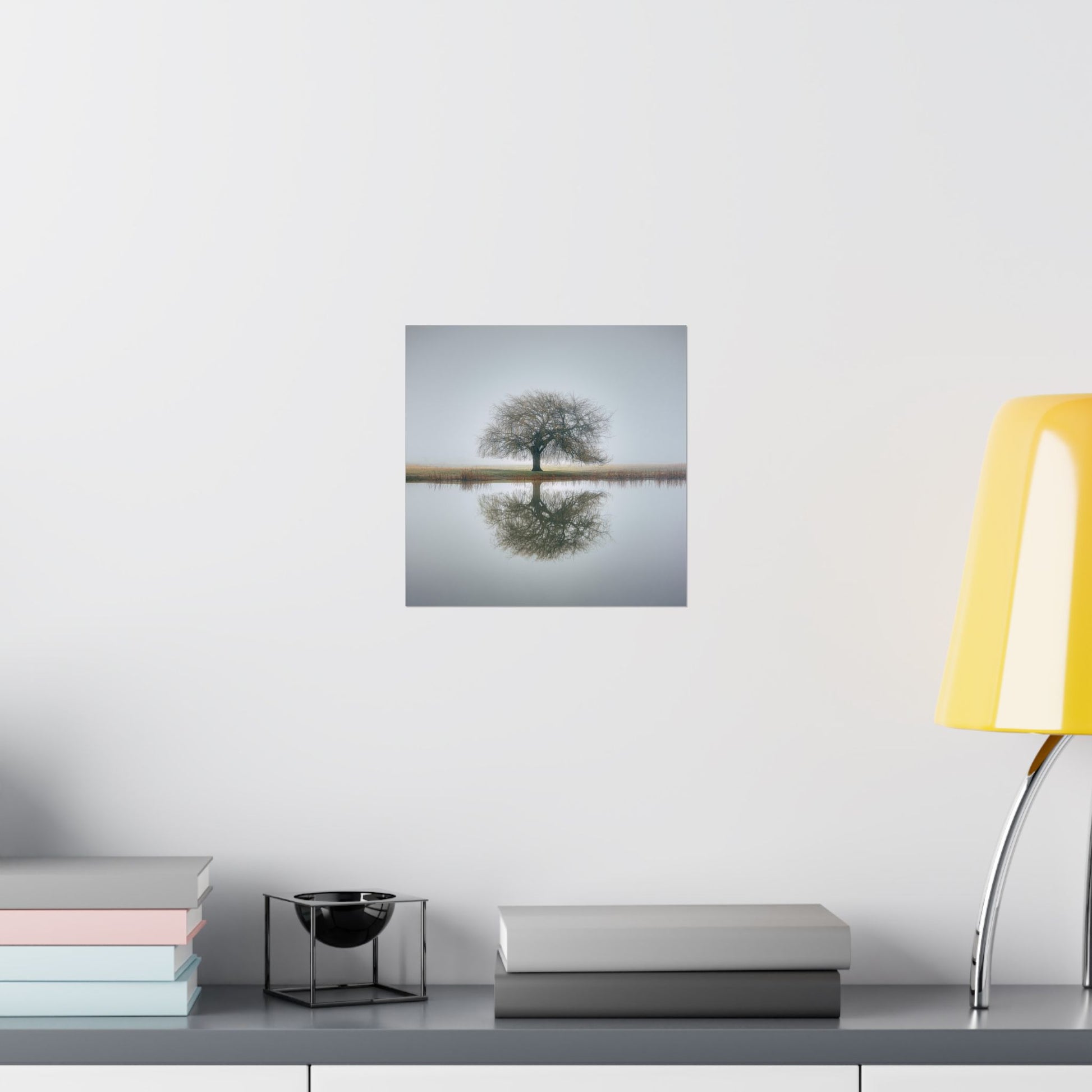 Framed artwork of a tree reflected in water on a wall above a desk with books and a lamp.