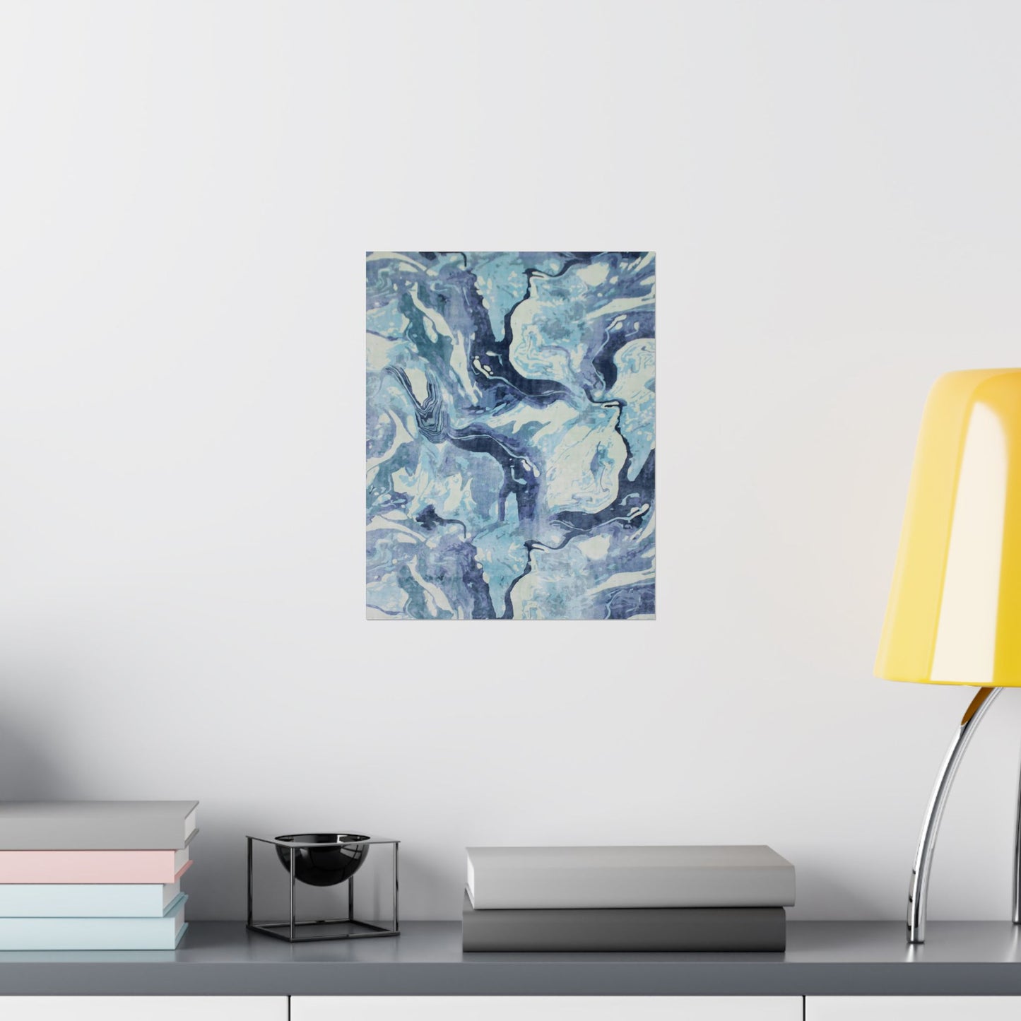Abstract blue and white painting on a wall above a shelf with books and a lamp.
