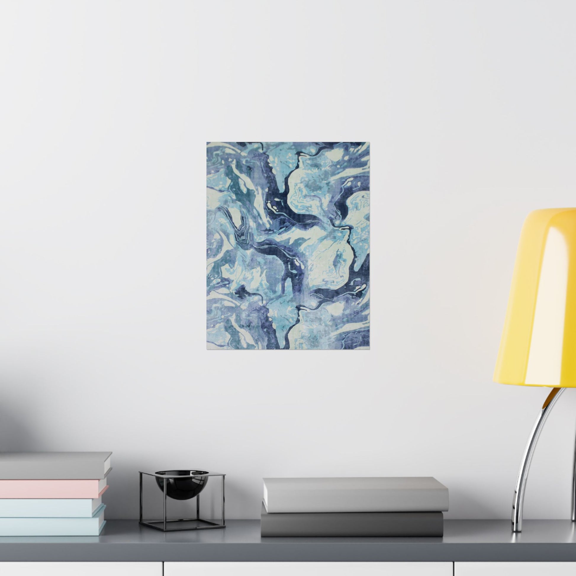 Abstract blue and white painting on a wall above a shelf with books and a lamp.
