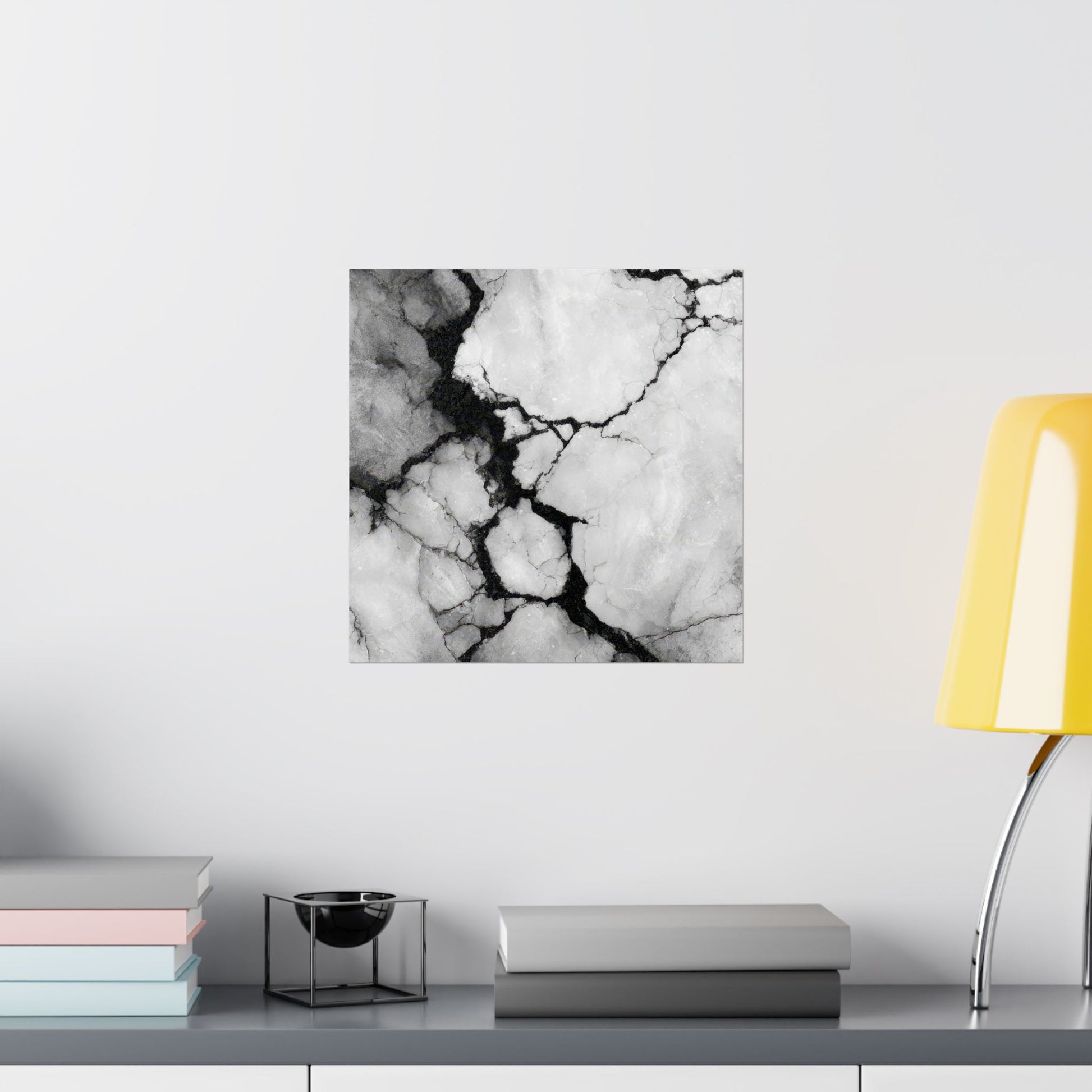 Black and white marble patterned wall art on a white wall with books and a lamp in the foreground.