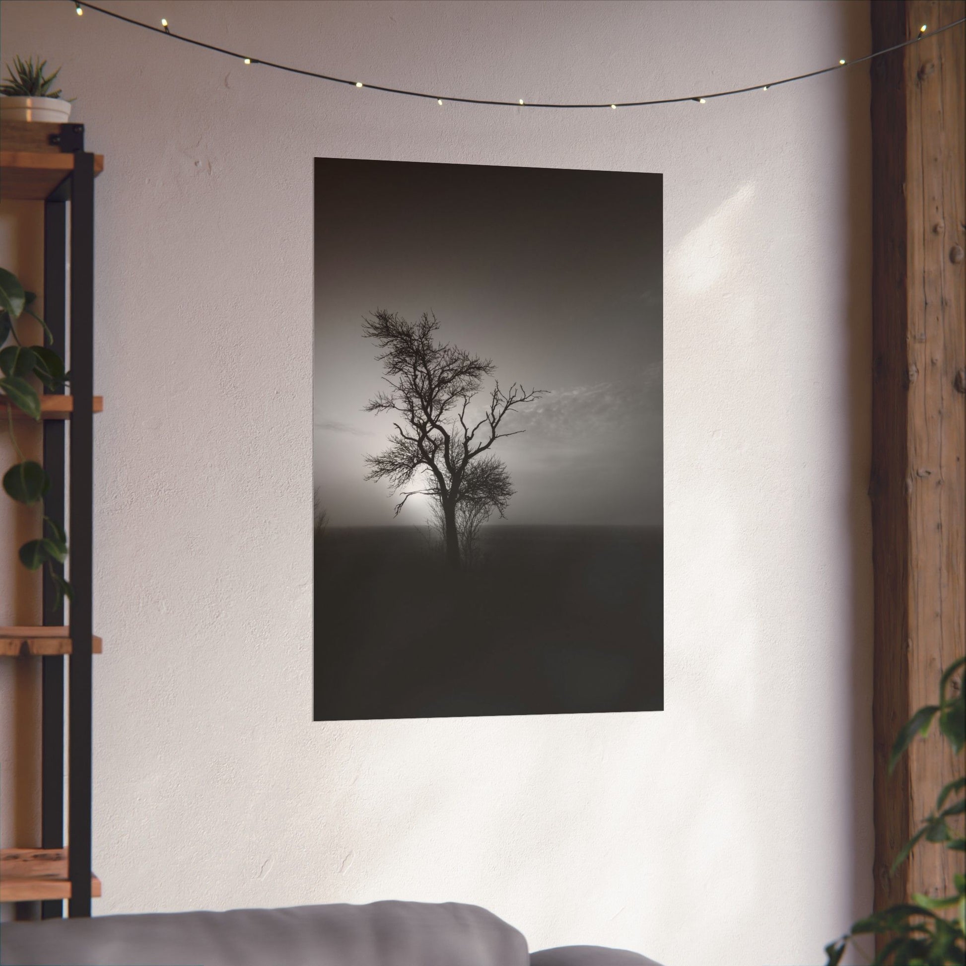 Poster of a lone tree in a field on a wall in a room with a shelf and plants.