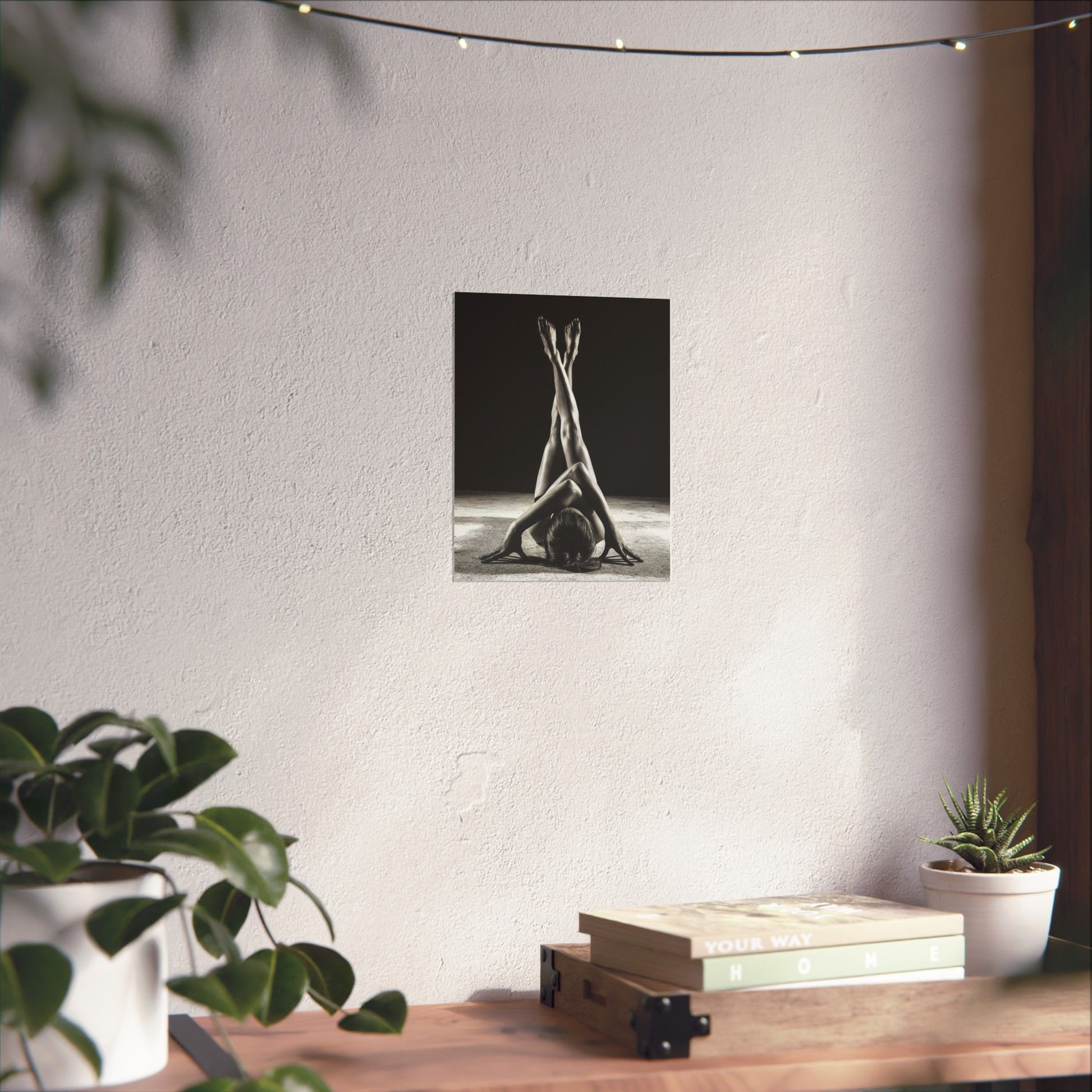 Yoga-themed wall art on a white wall with plants and books on a table below.