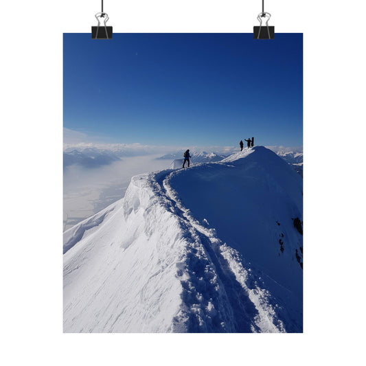 Two people standing on a snowy mountain peak with a clear blue sky.