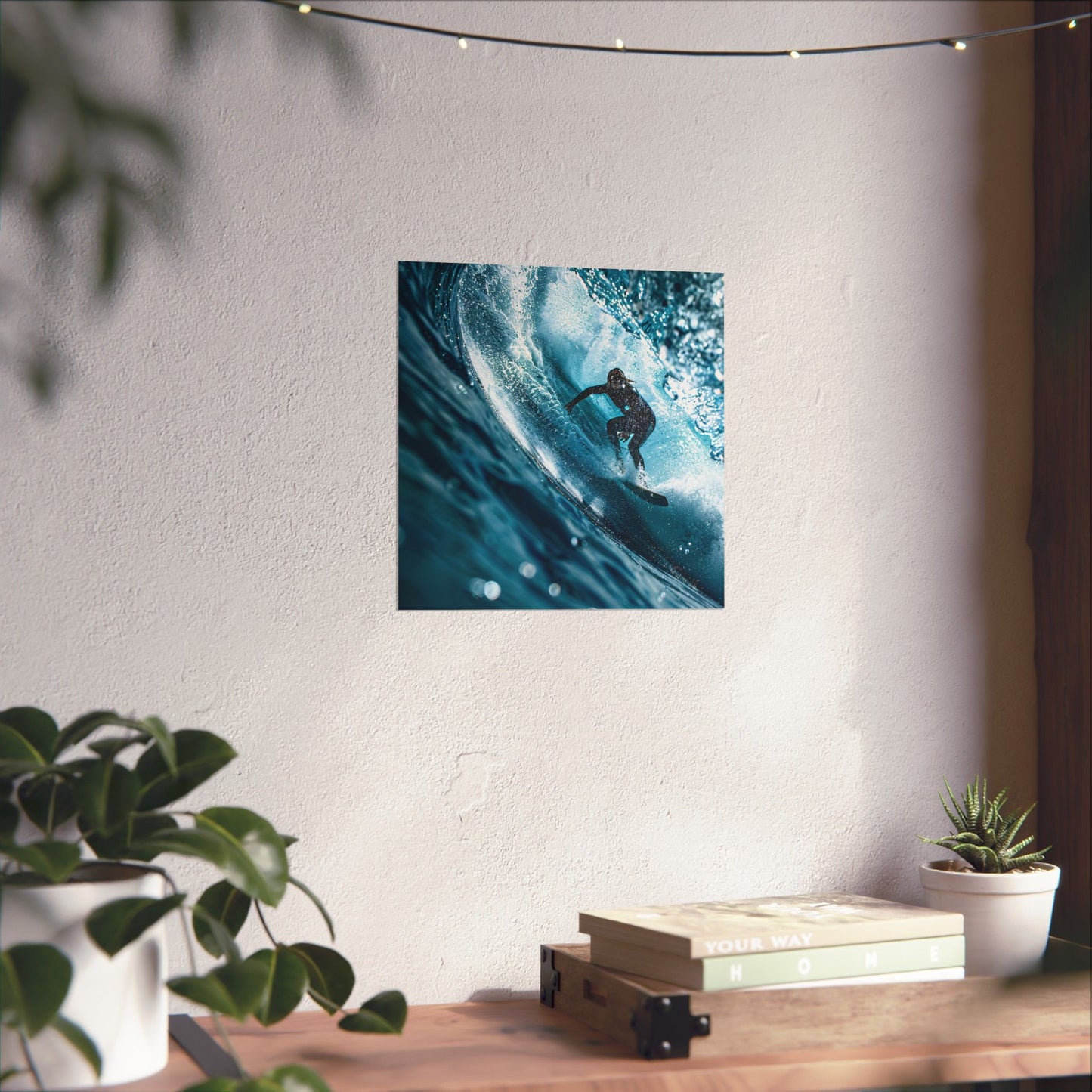 Poster of a surfer on a wave hanging on a wall above a wooden desk with plants.