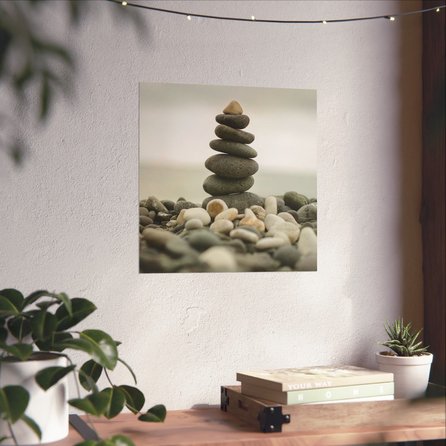 Stack of stones on a wall with plants and books on a table below.