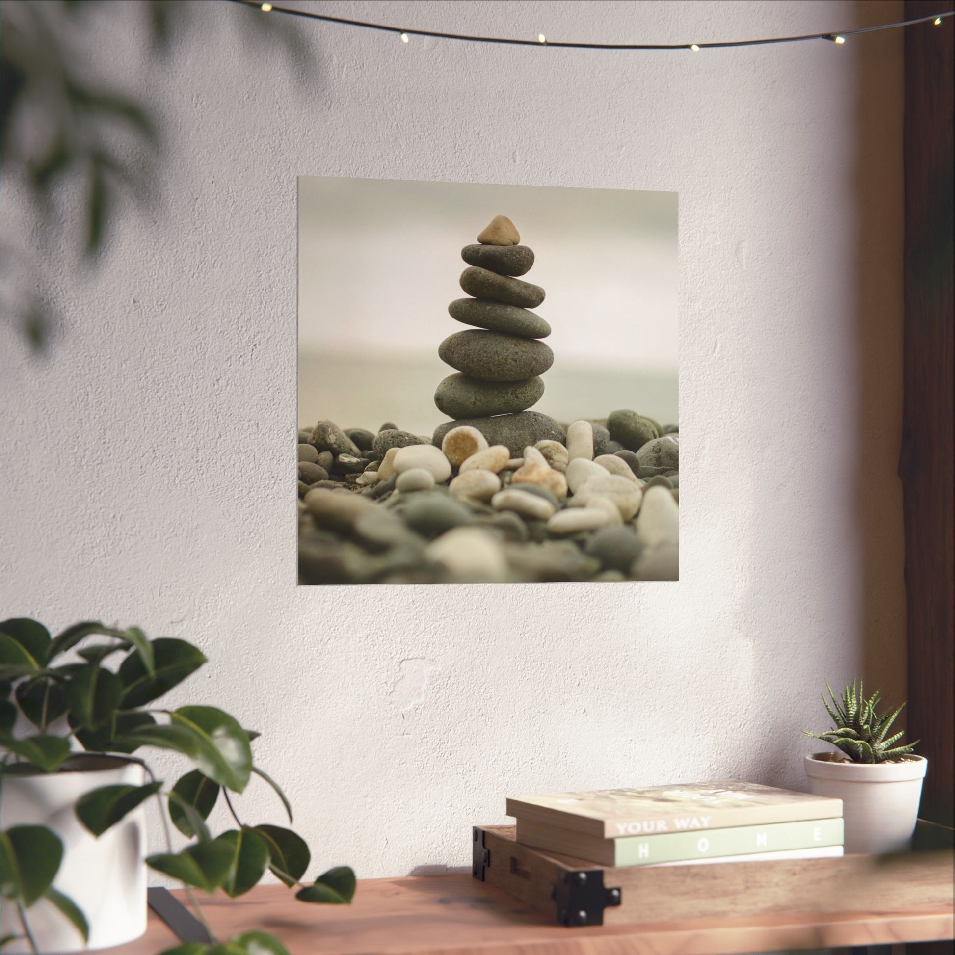 Stack of stones on a wall with plants and books on a table below.