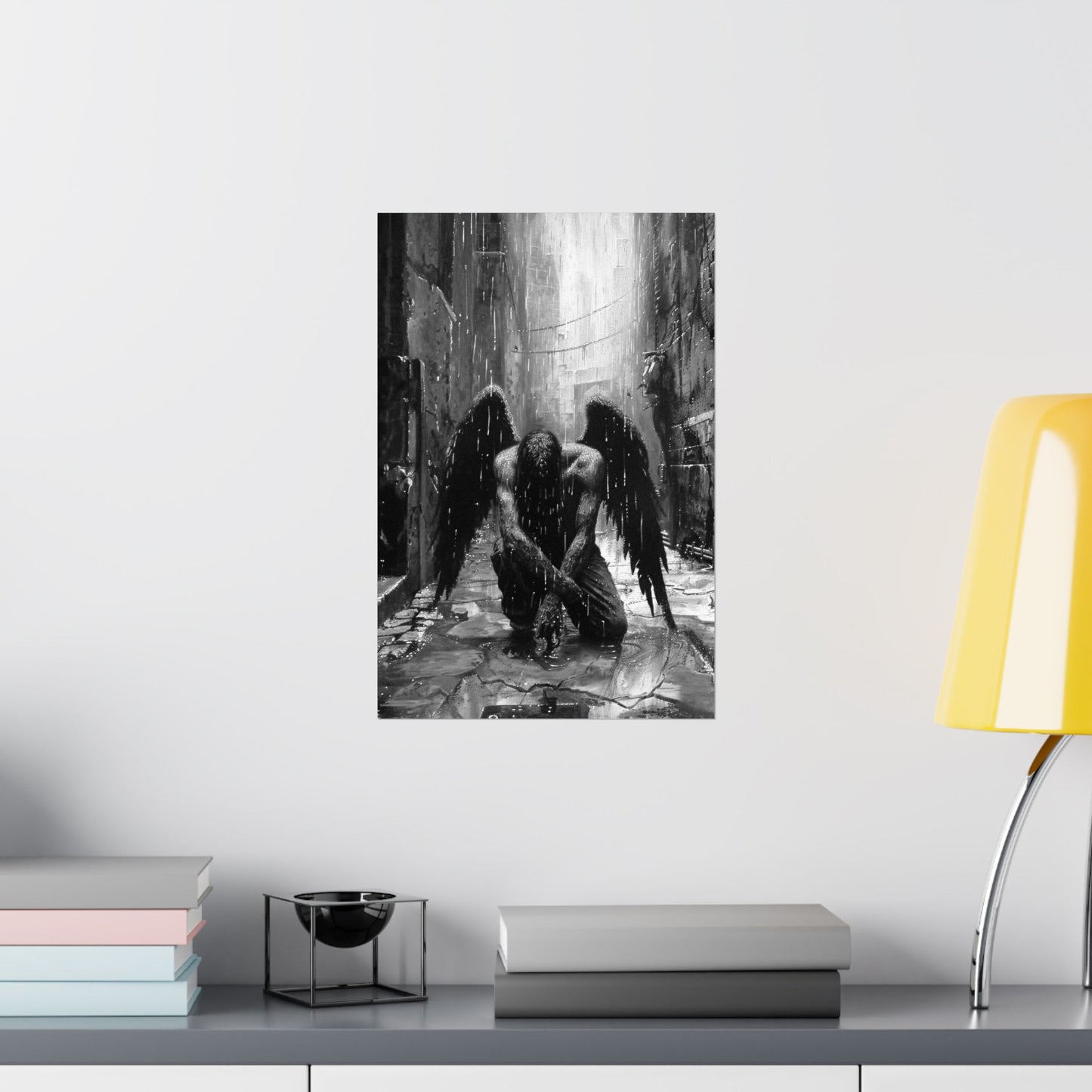 Framed artwork of an angel and demon in a dark alleyway on a wall above a shelf with books and a lamp.