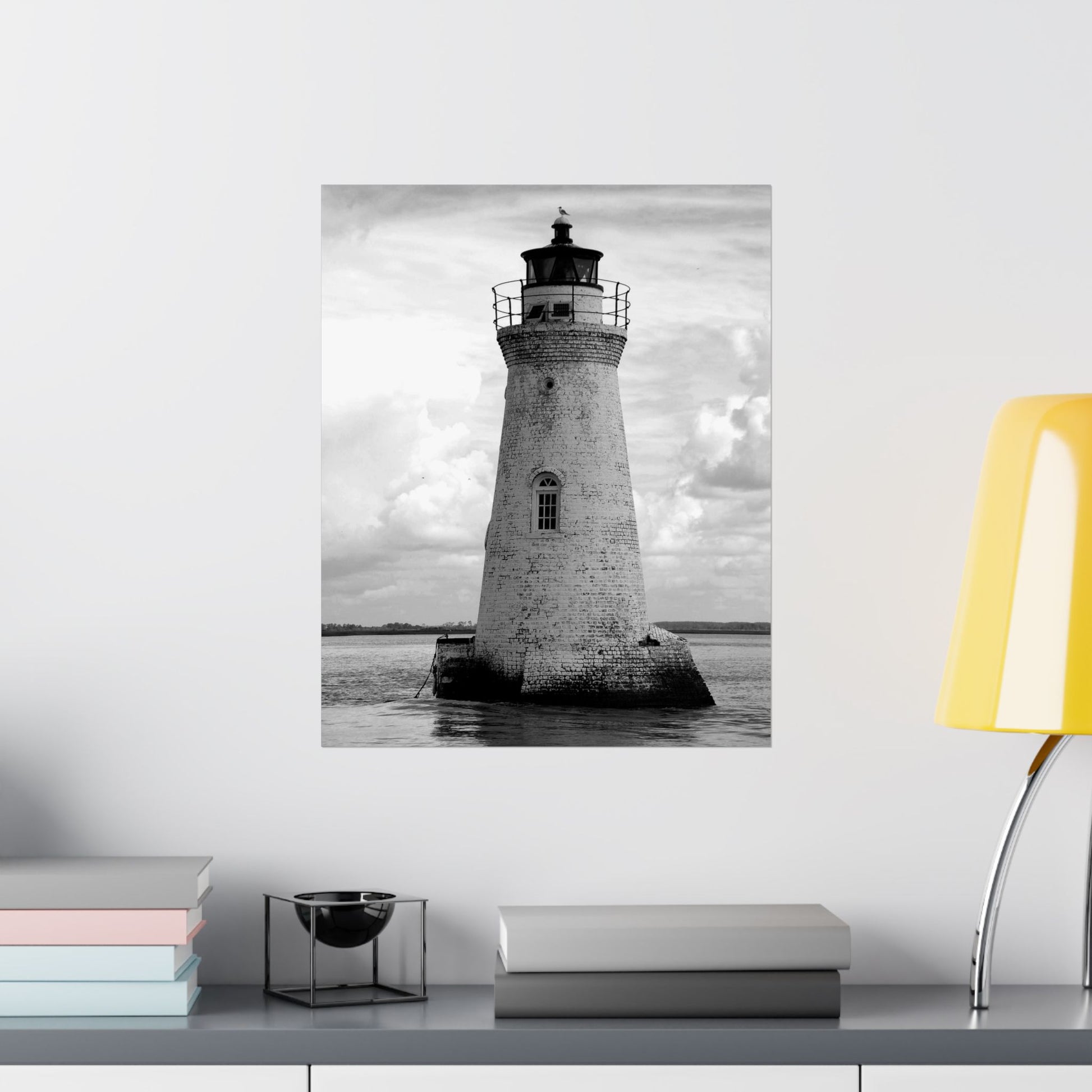Poster of a lighthouse on a wall above a shelf with books and decor items.