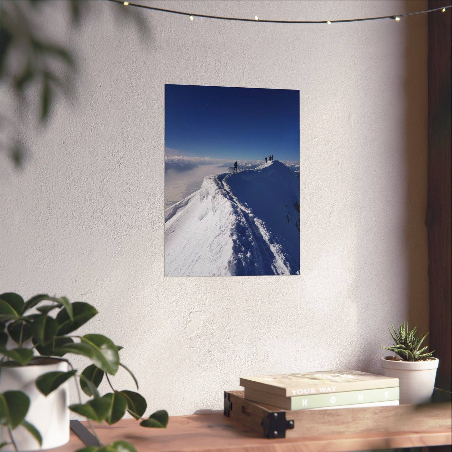 Poster of a snowy landscape on a wall above a wooden desk with plants and books.