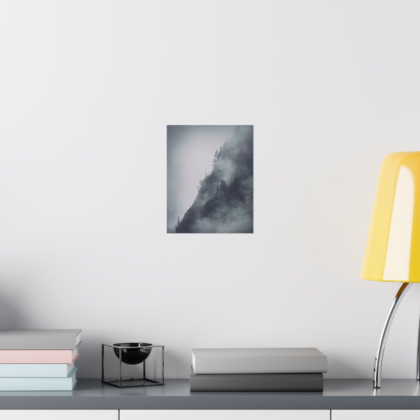 Framed artwork of a mountain landscape on a wall above a desk with books and a lamp.