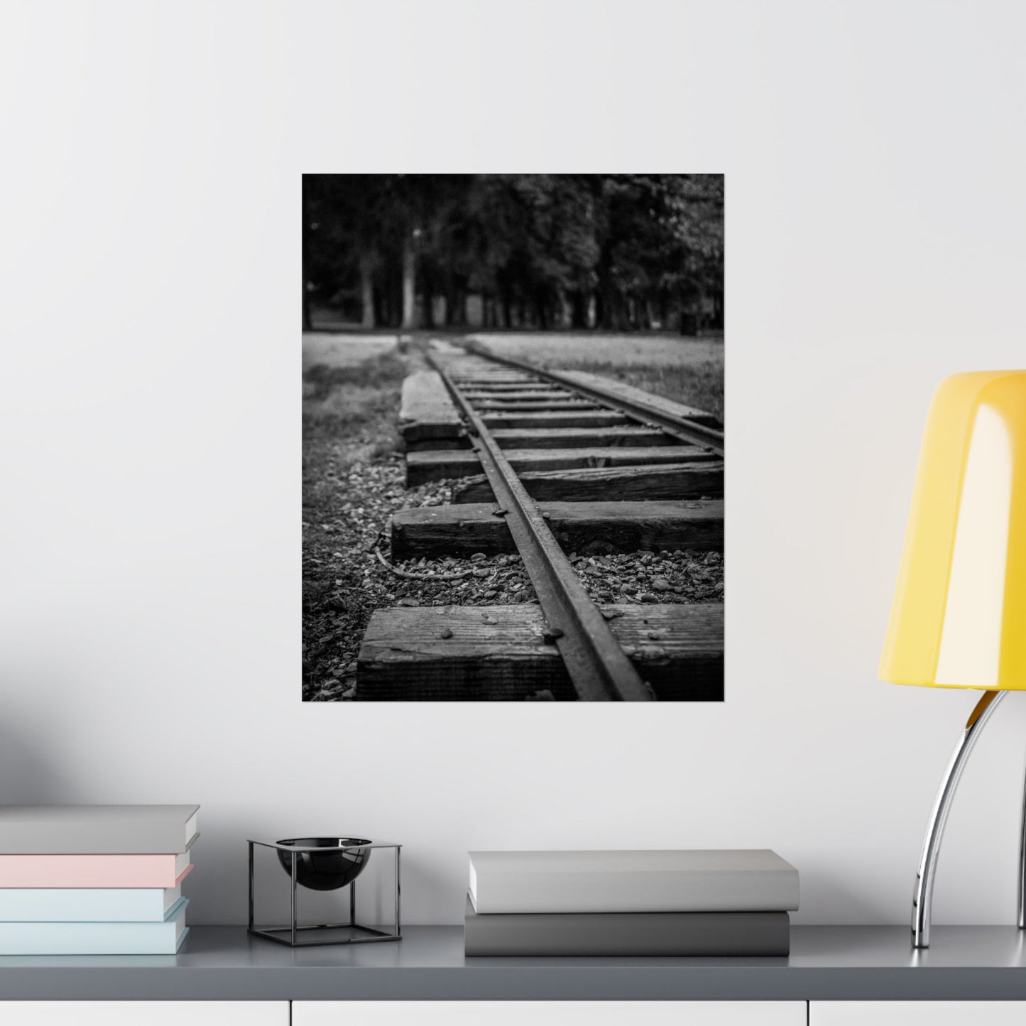Framed black and white photograph of a railway track on a wall above a shelf with books and a lamp.
