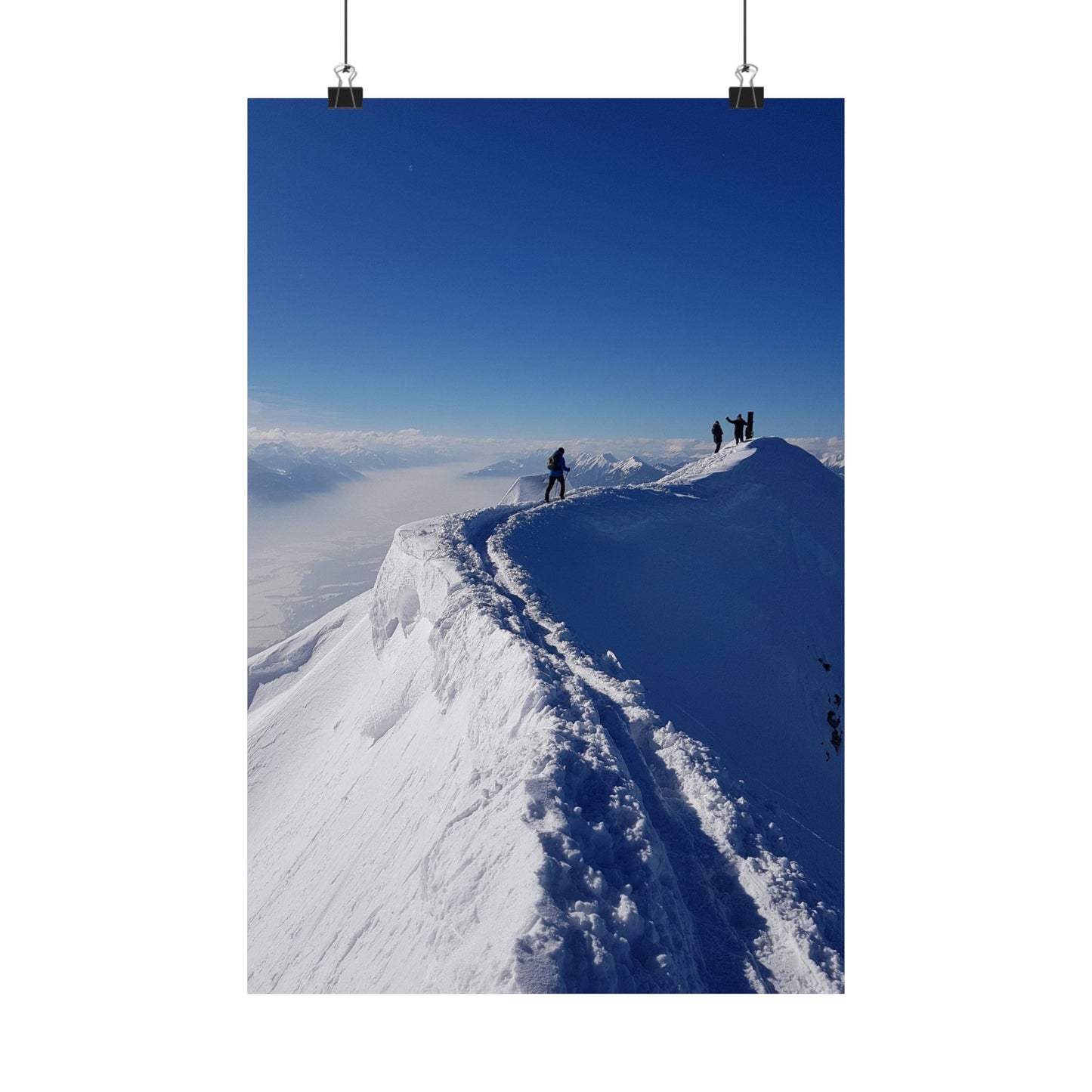 Two people standing on a snow-covered mountain peak with a clear blue sky.