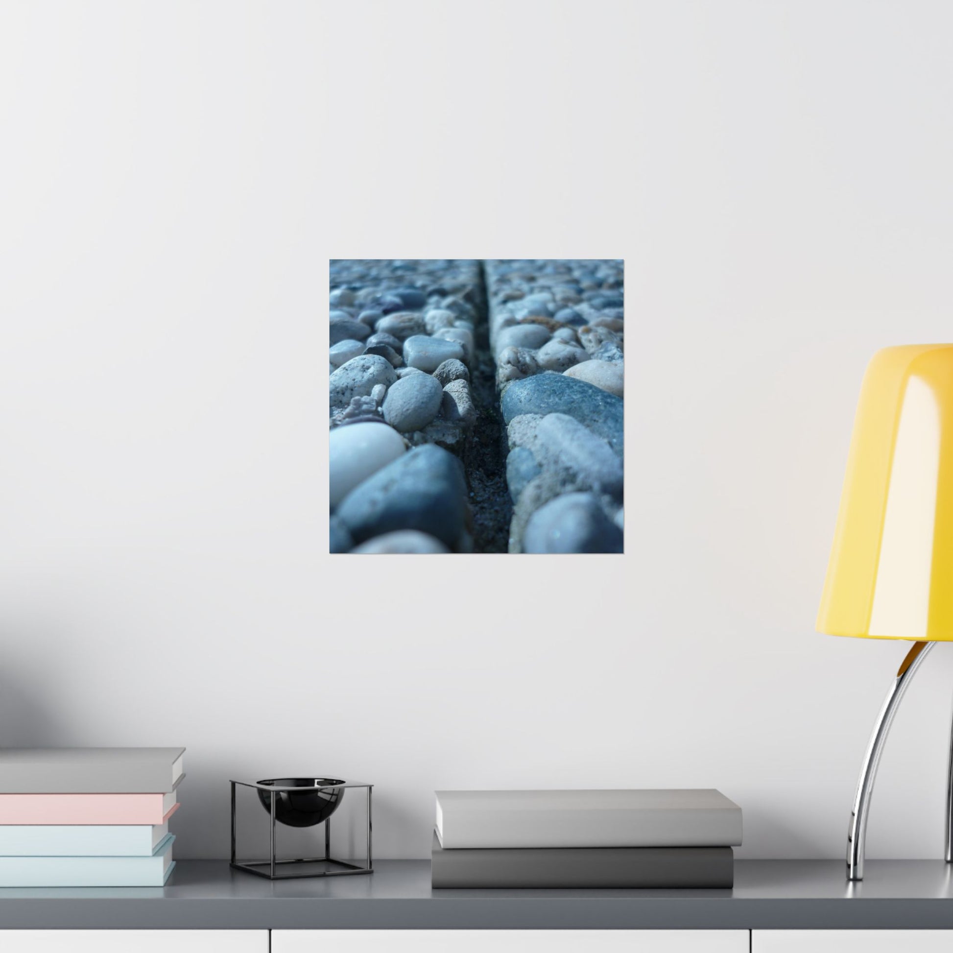 Wall art of pebbles on a white wall above a shelf with books and a lamp.