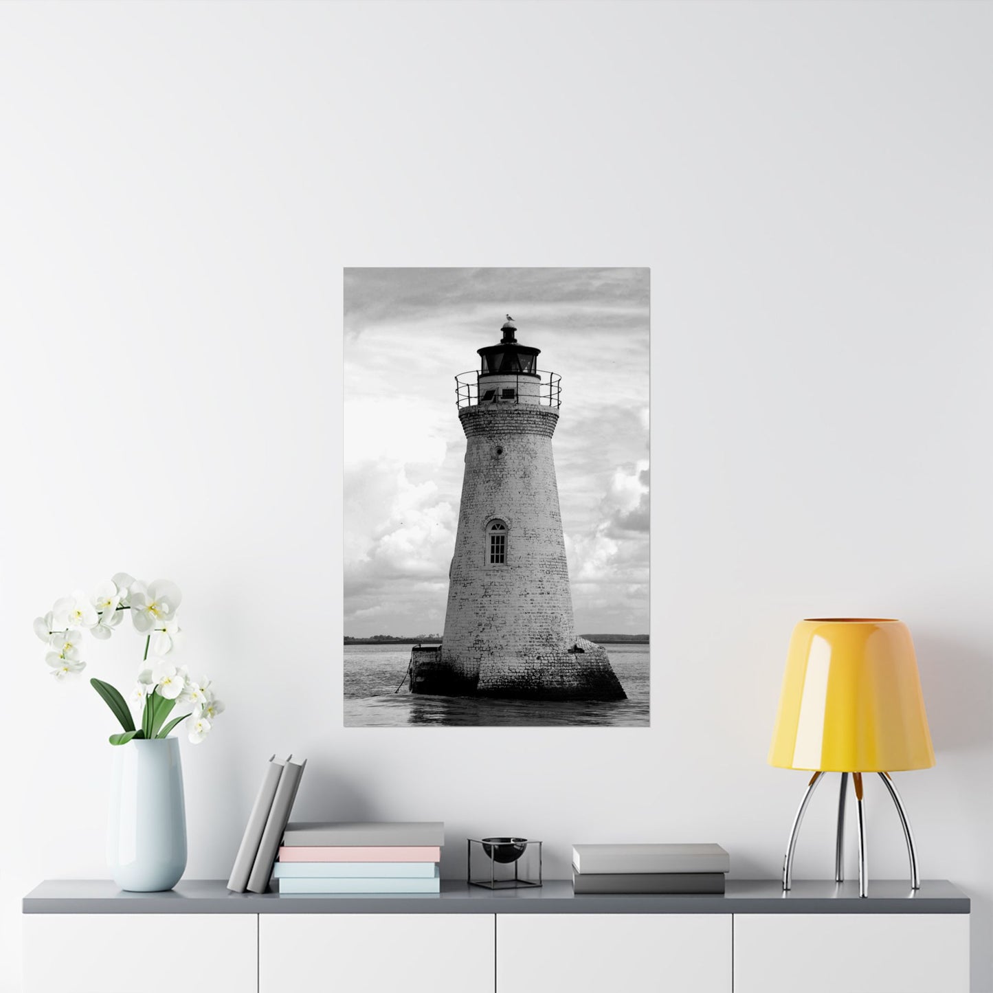 Framed black and white lighthouse print on a wall above a shelf with decor items.