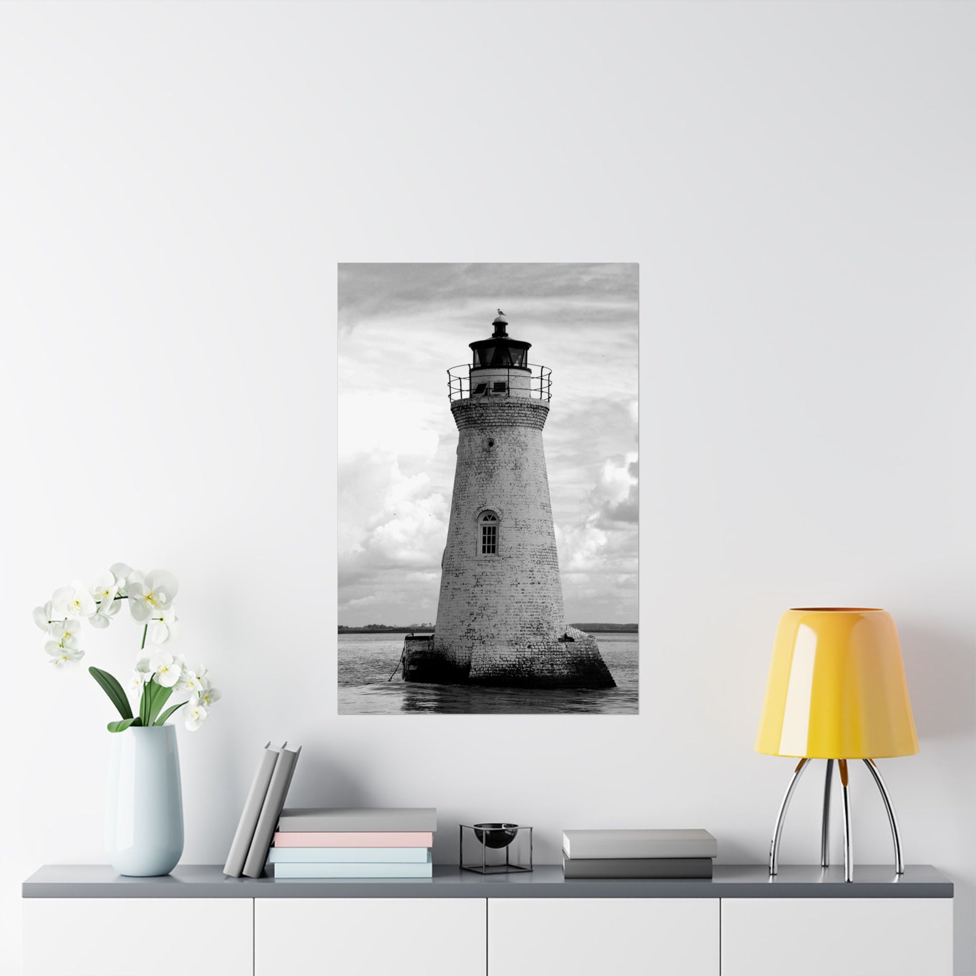 Framed black and white lighthouse print on a wall above a shelf with decor items.