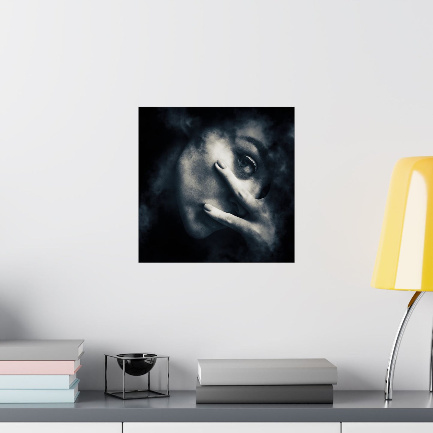 Framed artwork of a stylized face on a wall above a desk with books and a lamp.