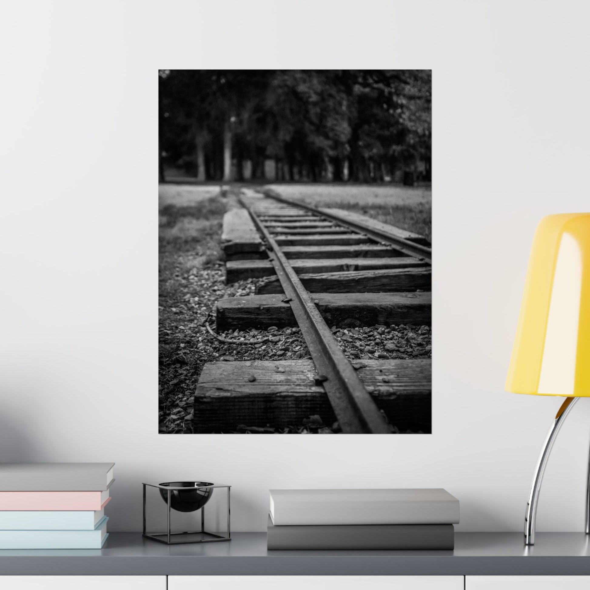 Framed black and white photo of a railway track on a wall above a shelf with books and decor items.