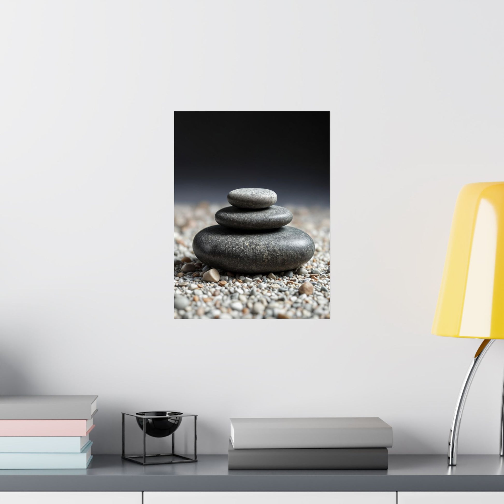 Wall art of stacked stones on pebbles with a yellow lamp and books on a shelf.