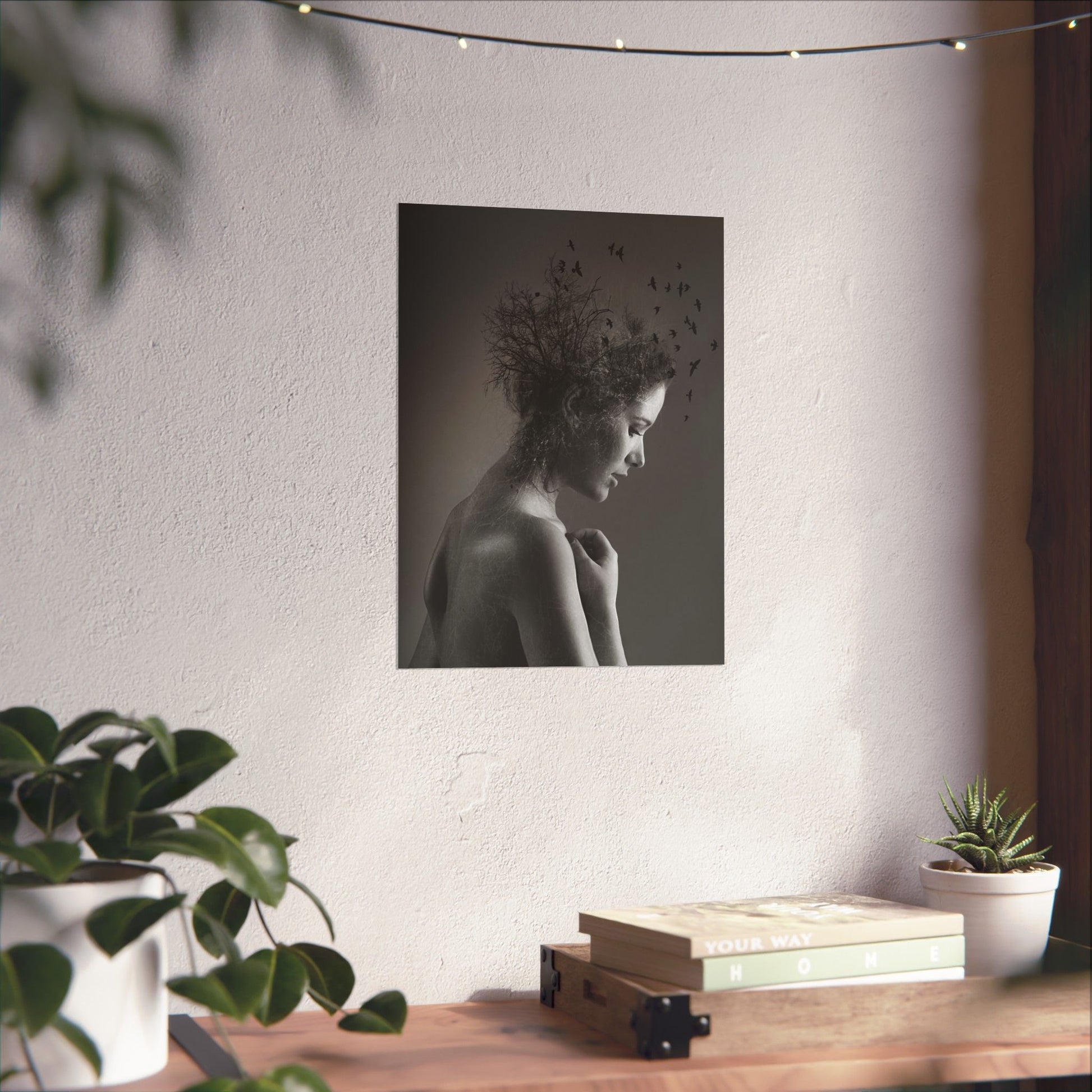 Black and white portrait of a woman with flowers on her head hanging on a wall above a wooden desk with plants.