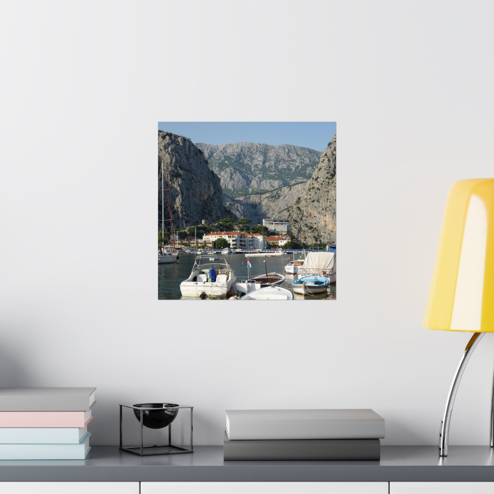 Framed photograph of a coastal scene with boats and mountains on a wall above a shelf.
