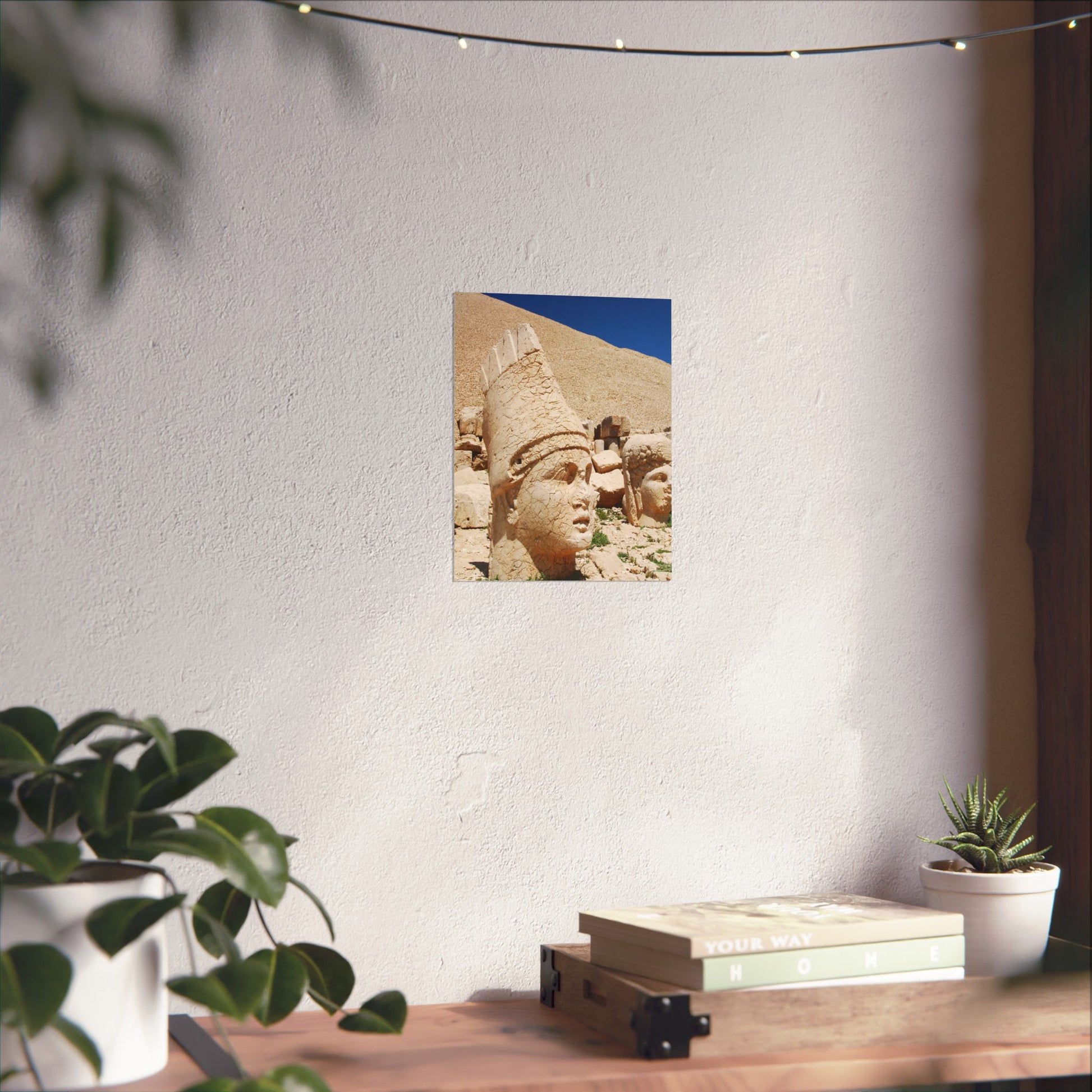 Poster of ancient sculpture on a wall with plants and books on a table below.