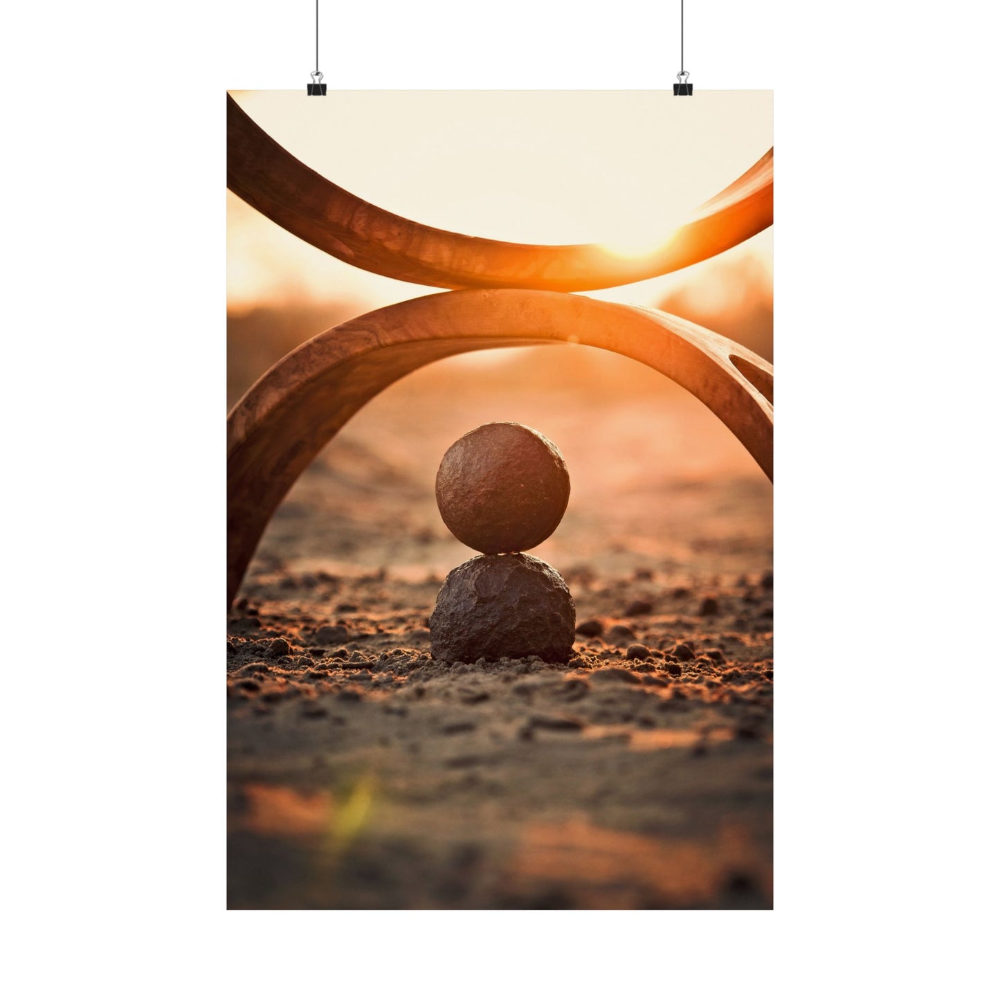 Two large circular metal structures with a small stone balanced on the ground at sunset.