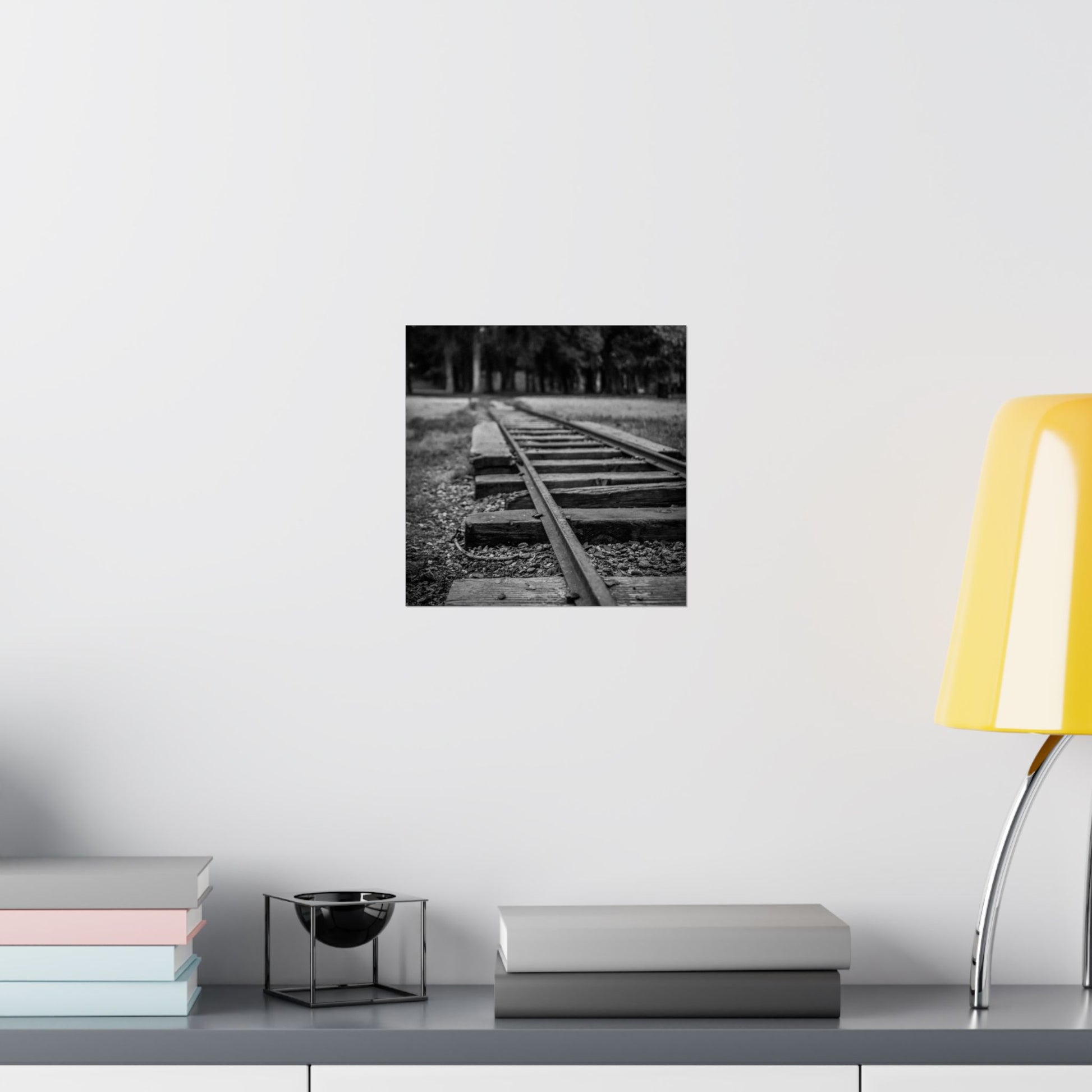 Black and white photograph of a railway track on a wall above a desk with books and a lamp.