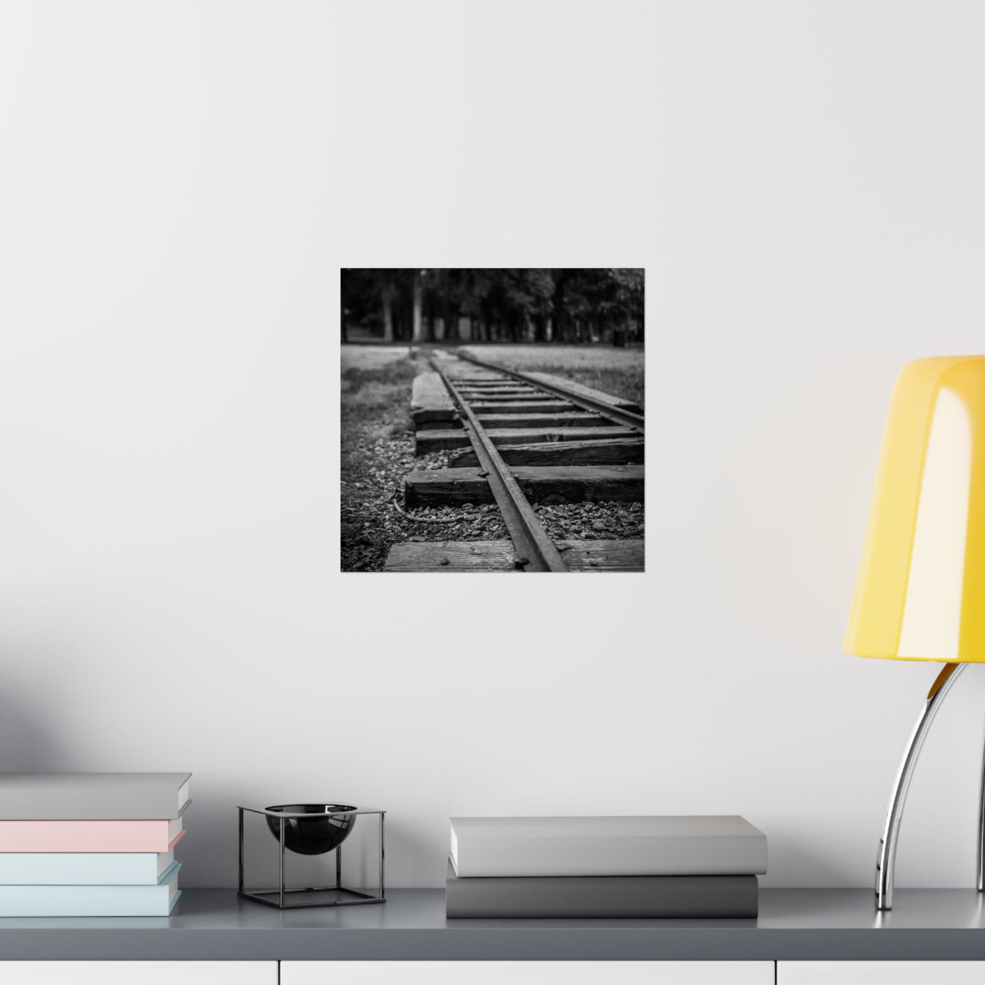 Black and white photograph of a railway track on a wall above a shelf with books and a lamp.