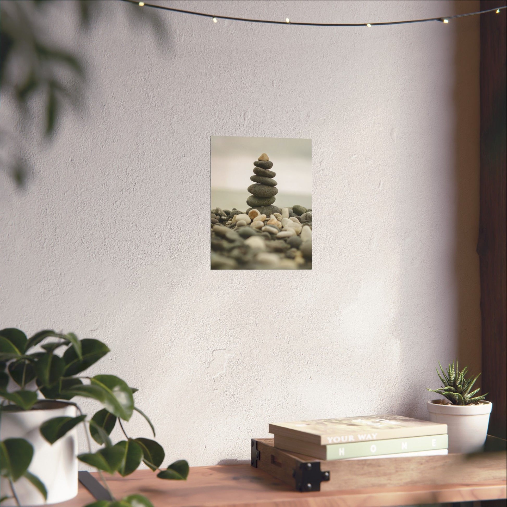 Stack of stones on a wall with plants and books on a table below.