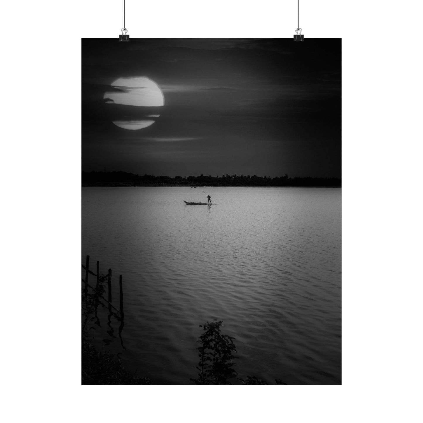 Black and white photo of a person in a boat on a lake with a large moon in the sky.