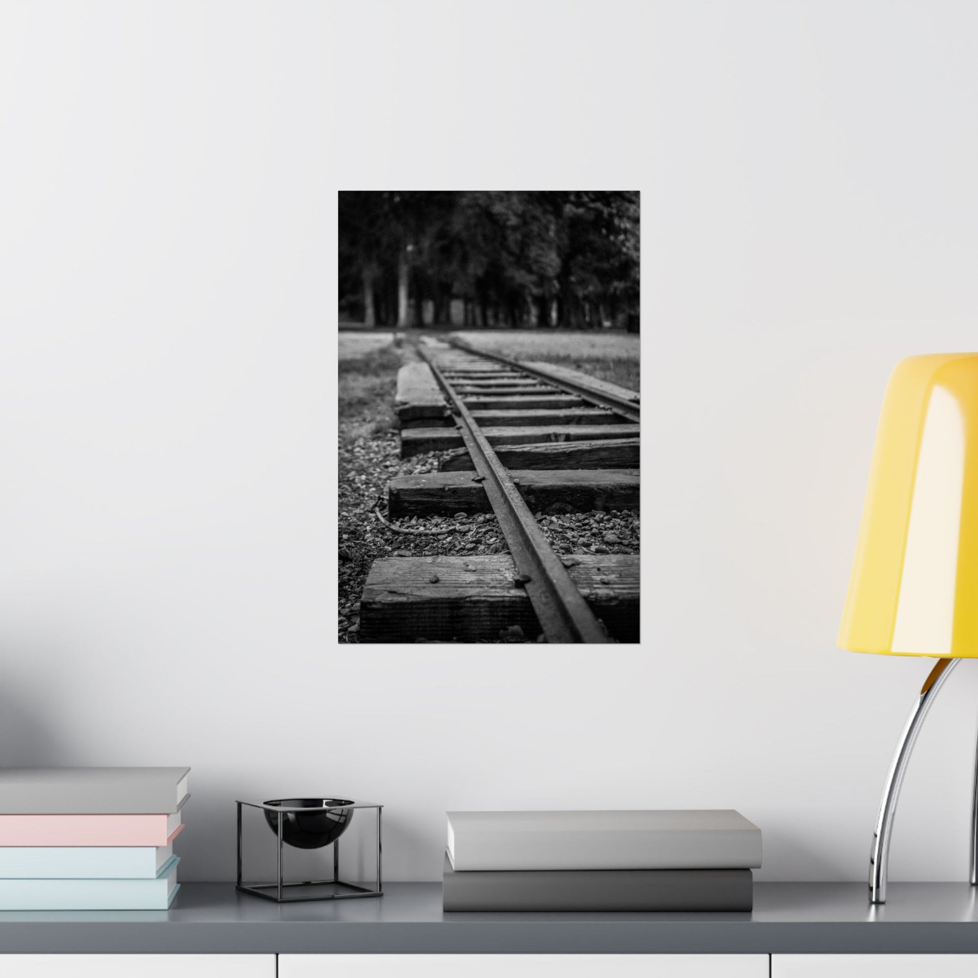 Framed black and white photo of a railway track on a wall above a shelf with books and decor.