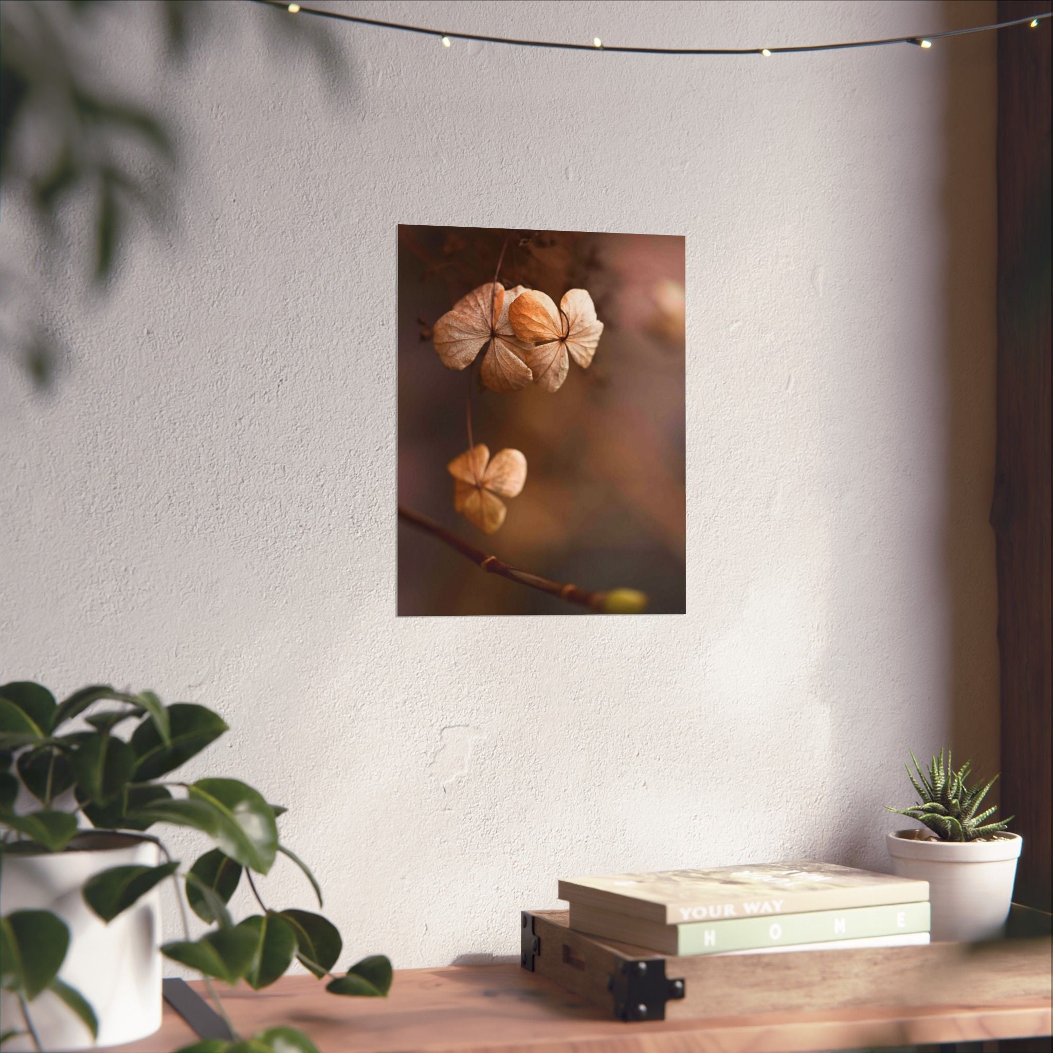 Decorative wall art of flowers on a white wall with plants and books on a table below.