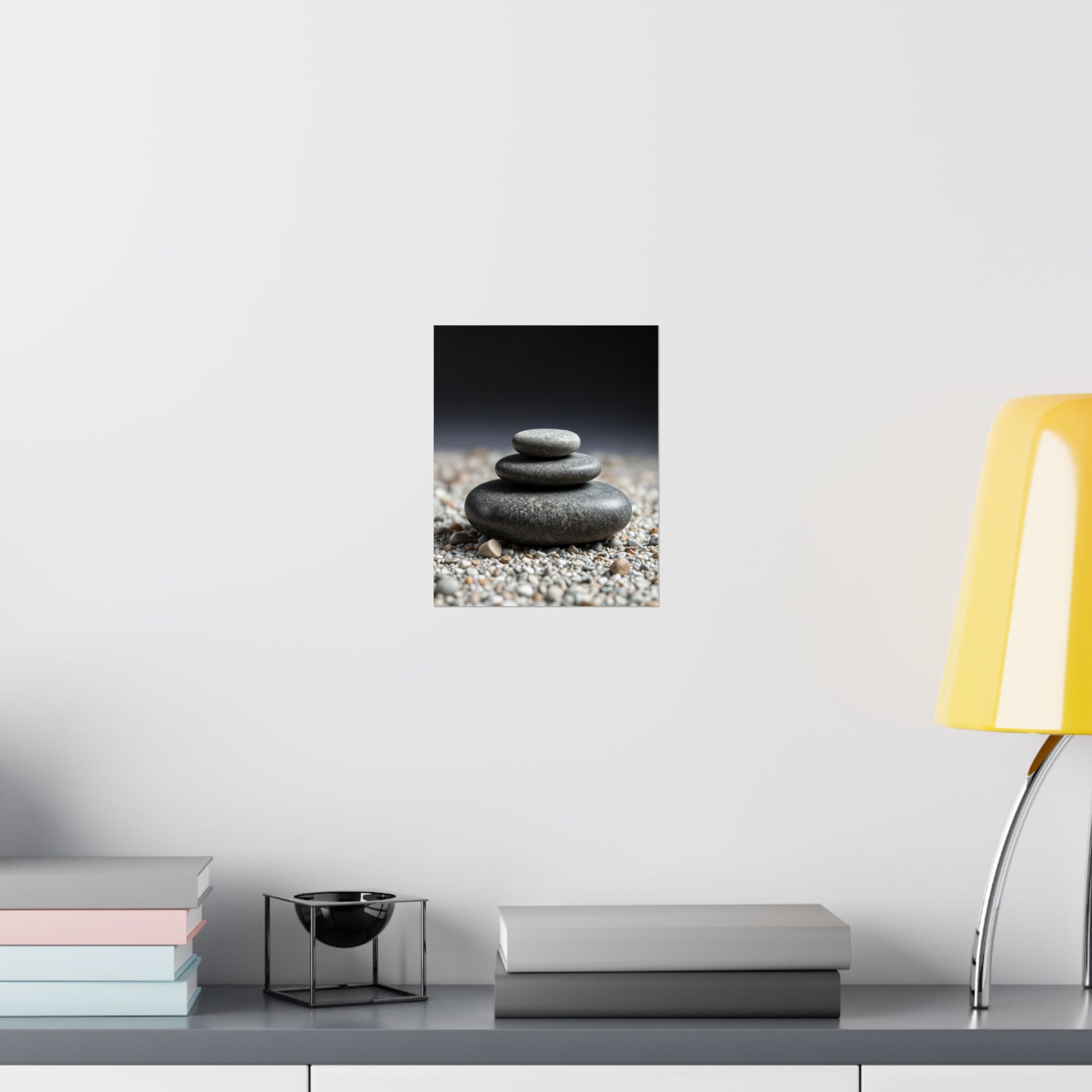 Wall art of stacked stones on pebbles with a yellow lamp and books on a shelf.