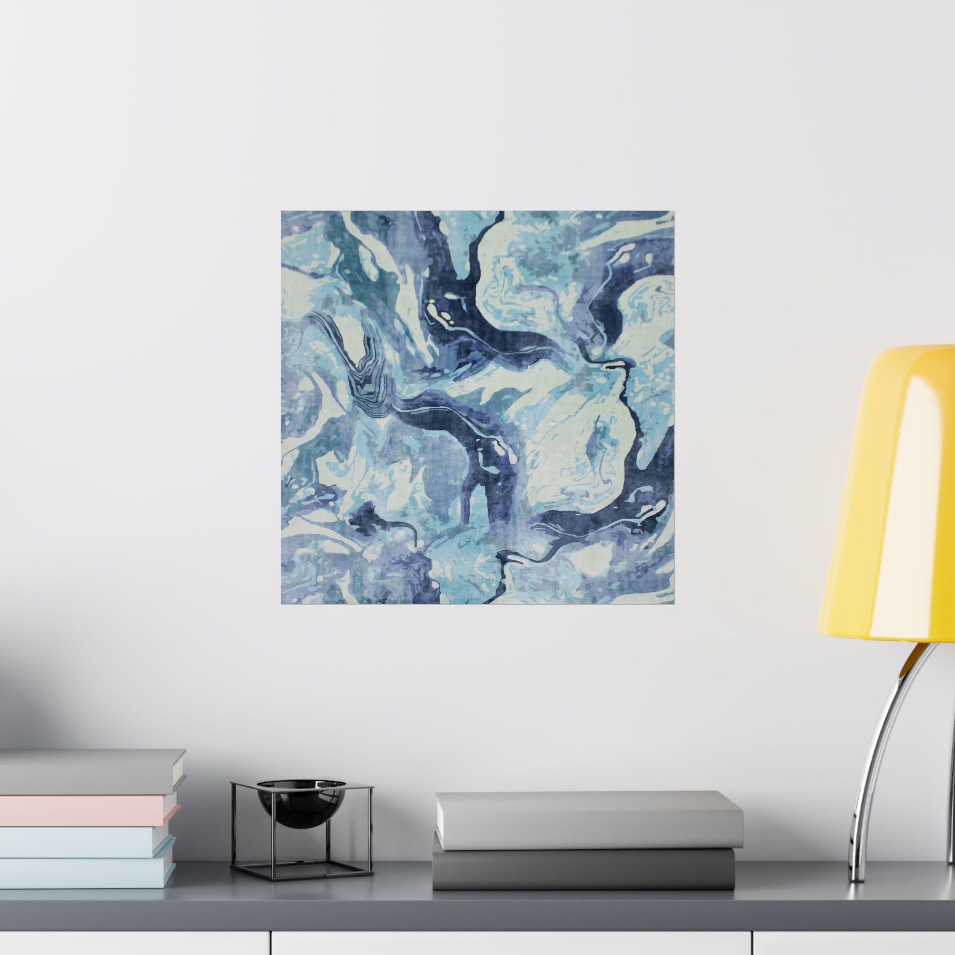 Abstract blue and white painting on a wall above a shelf with books and a lamp.