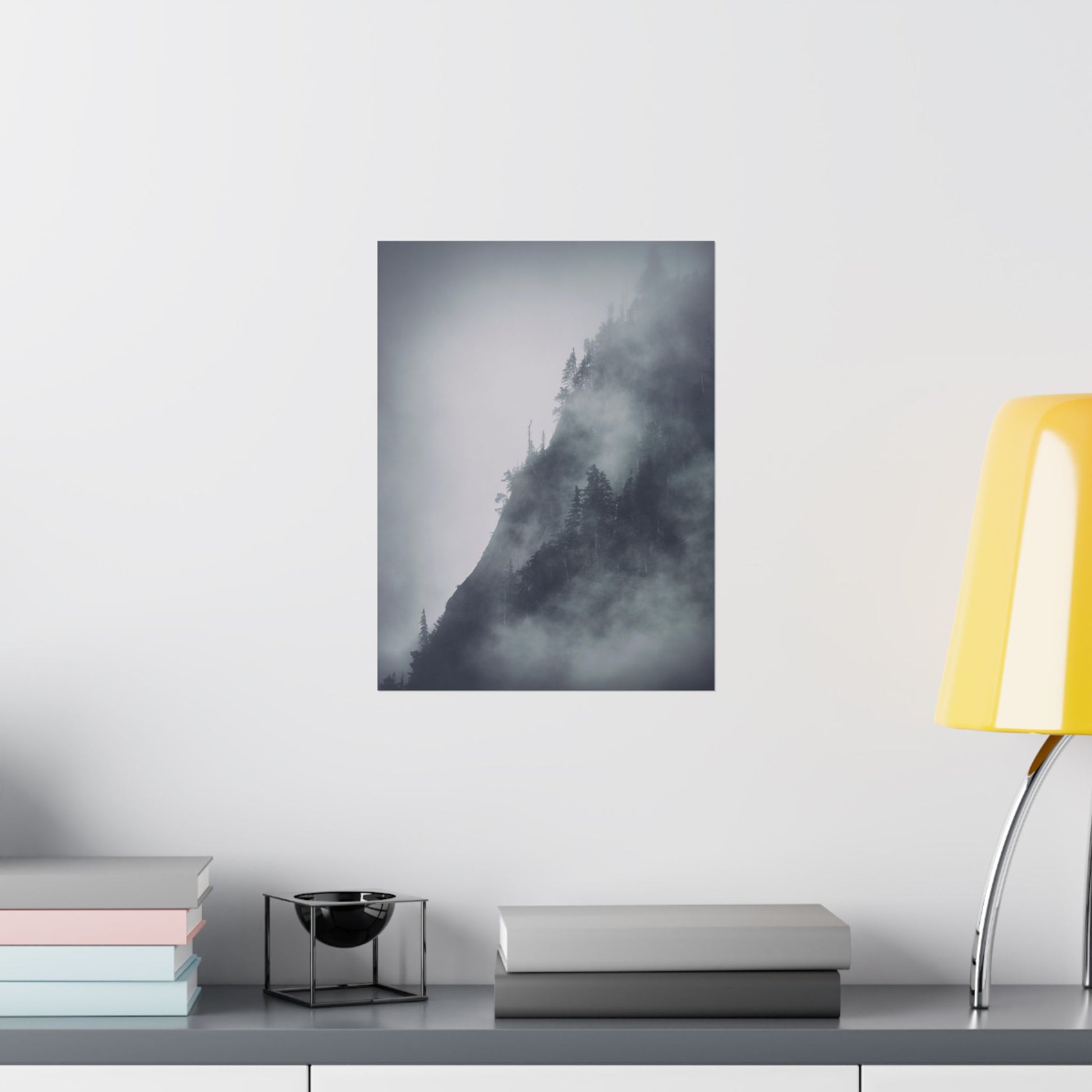 Framed black and white mountain landscape art on a wall above a desk with books and a lamp.