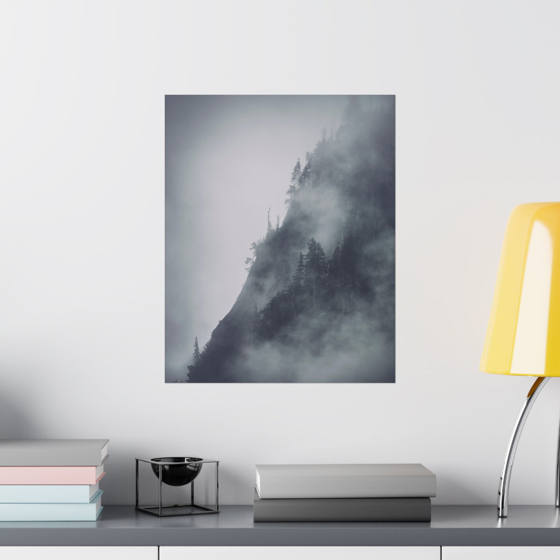 Framed black and white mountain landscape print on a wall above a desk with books and a lamp.