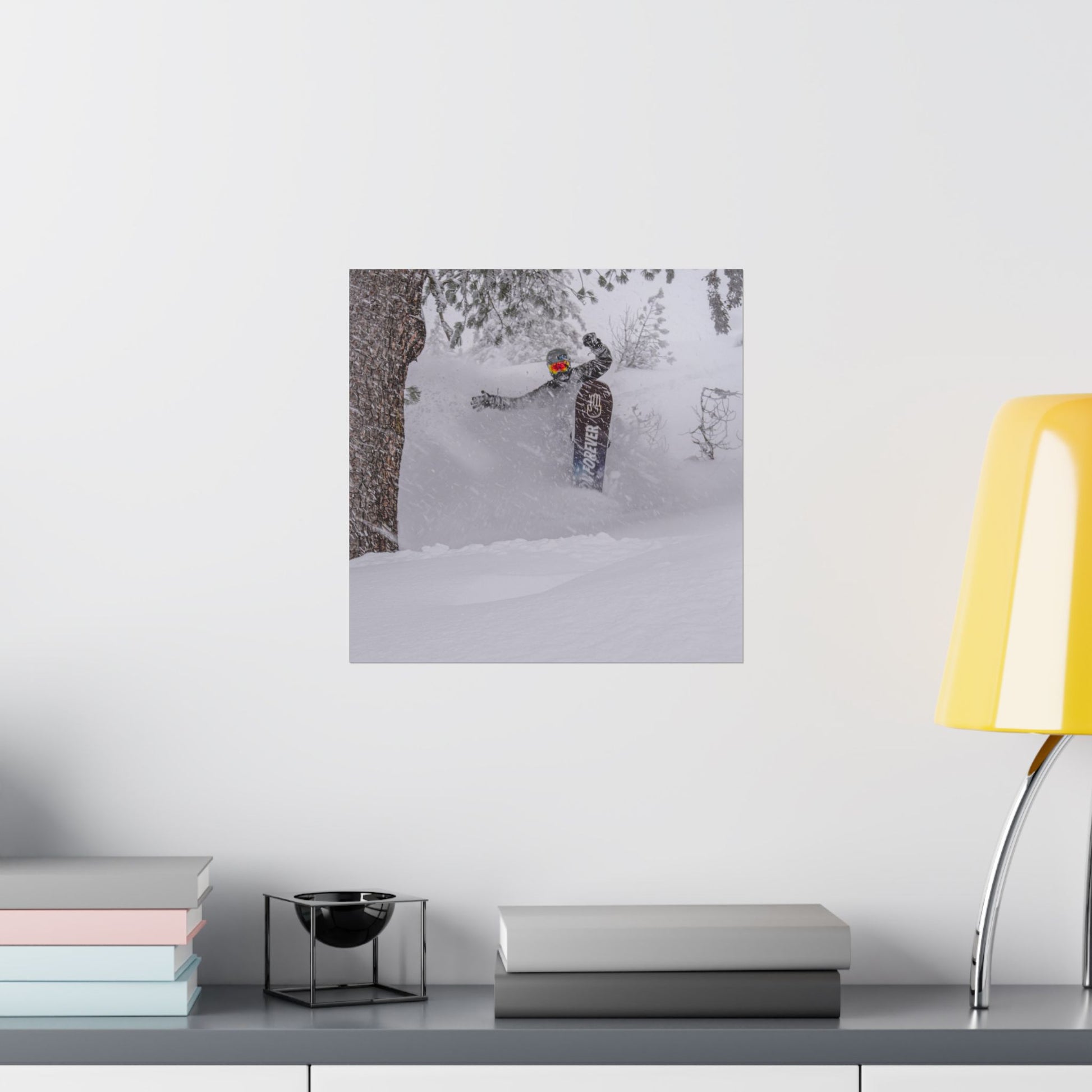 Poster of a person skiing on a snowy landscape above a desk with books and a lamp.