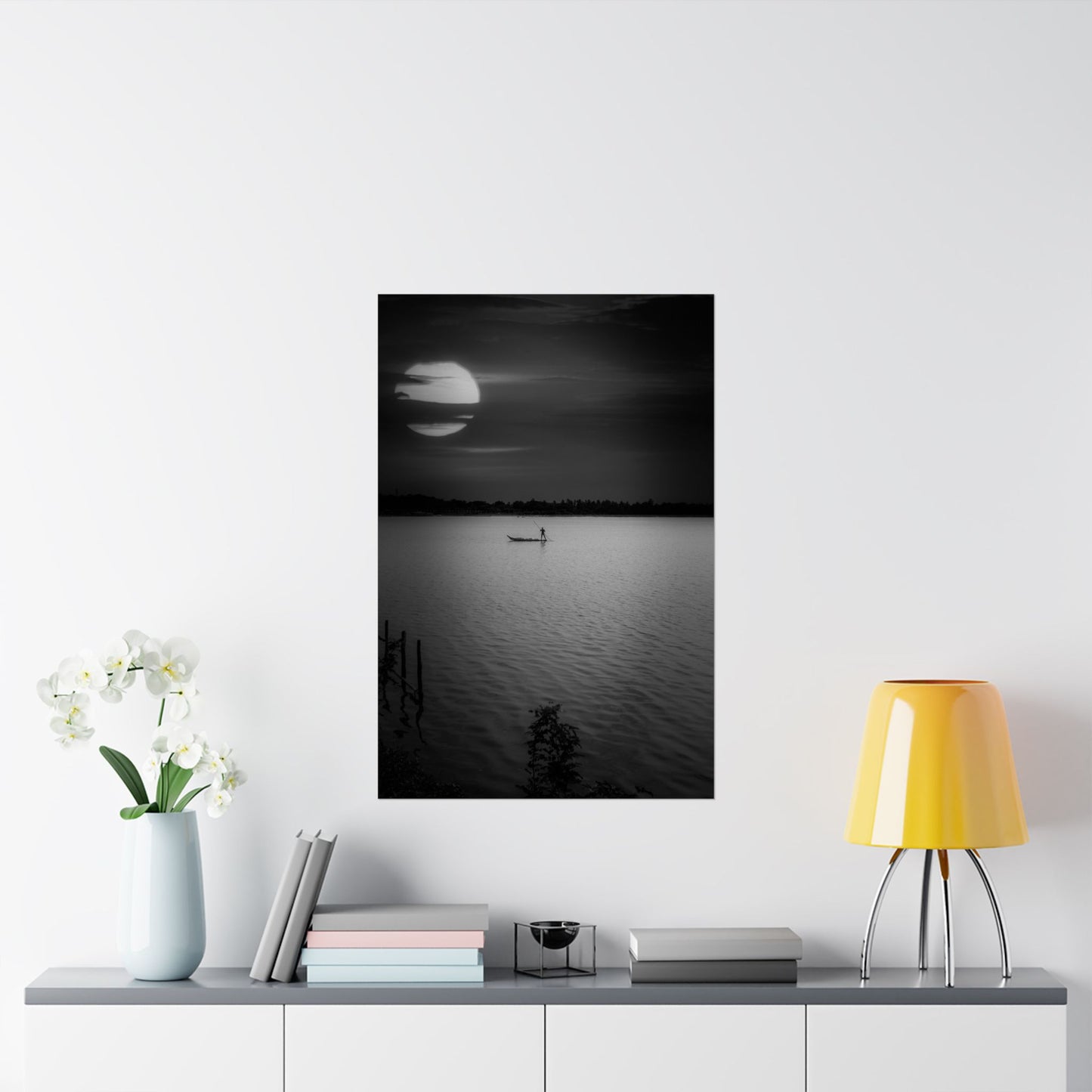Framed black and white artwork of a moonlit lake with a boat, displayed on a wall above a shelf.