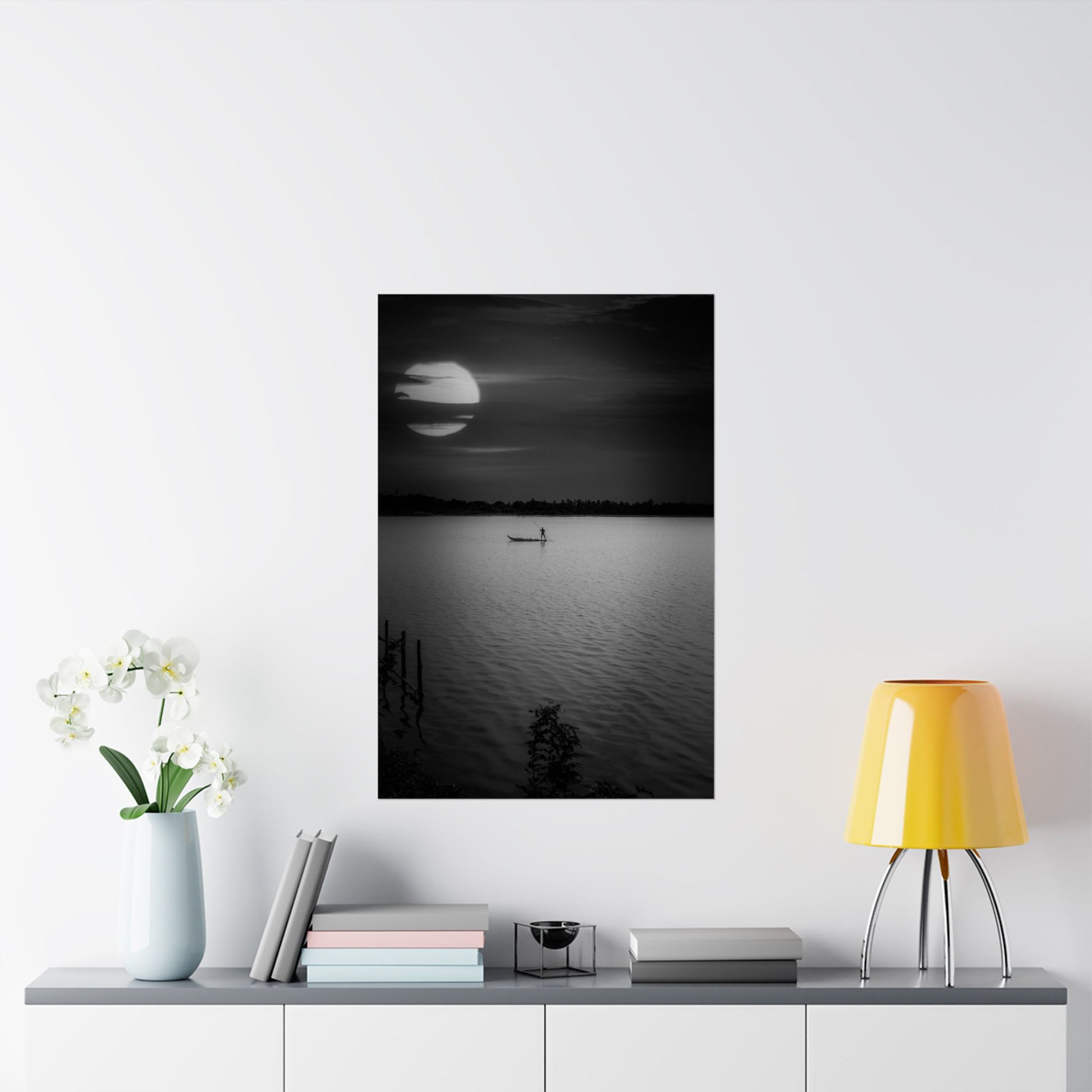 Framed black and white artwork of a moonlit lake with a boat, displayed on a wall above a shelf.